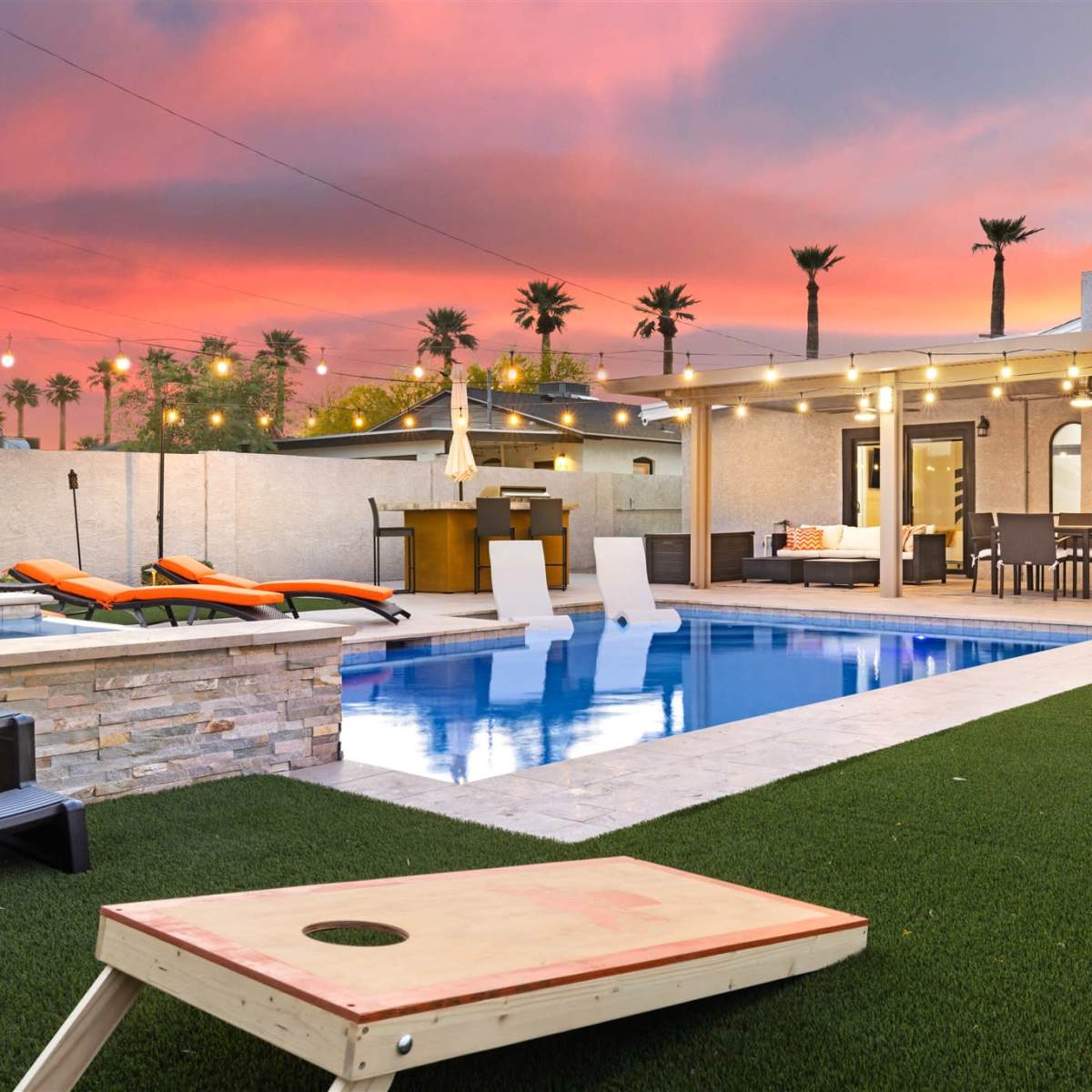 A backyard pool area with lounge chairs, a green lawn, and string lights against a sunset sky.
