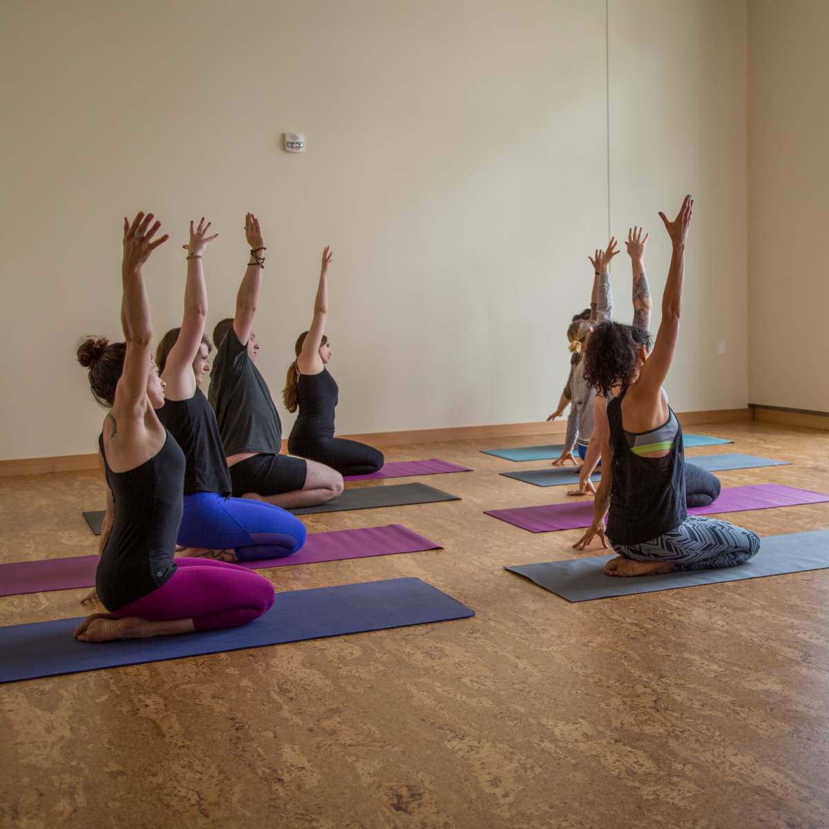 A group of individuals practices yoga in a spacious studio with large windows, using colorful mats.