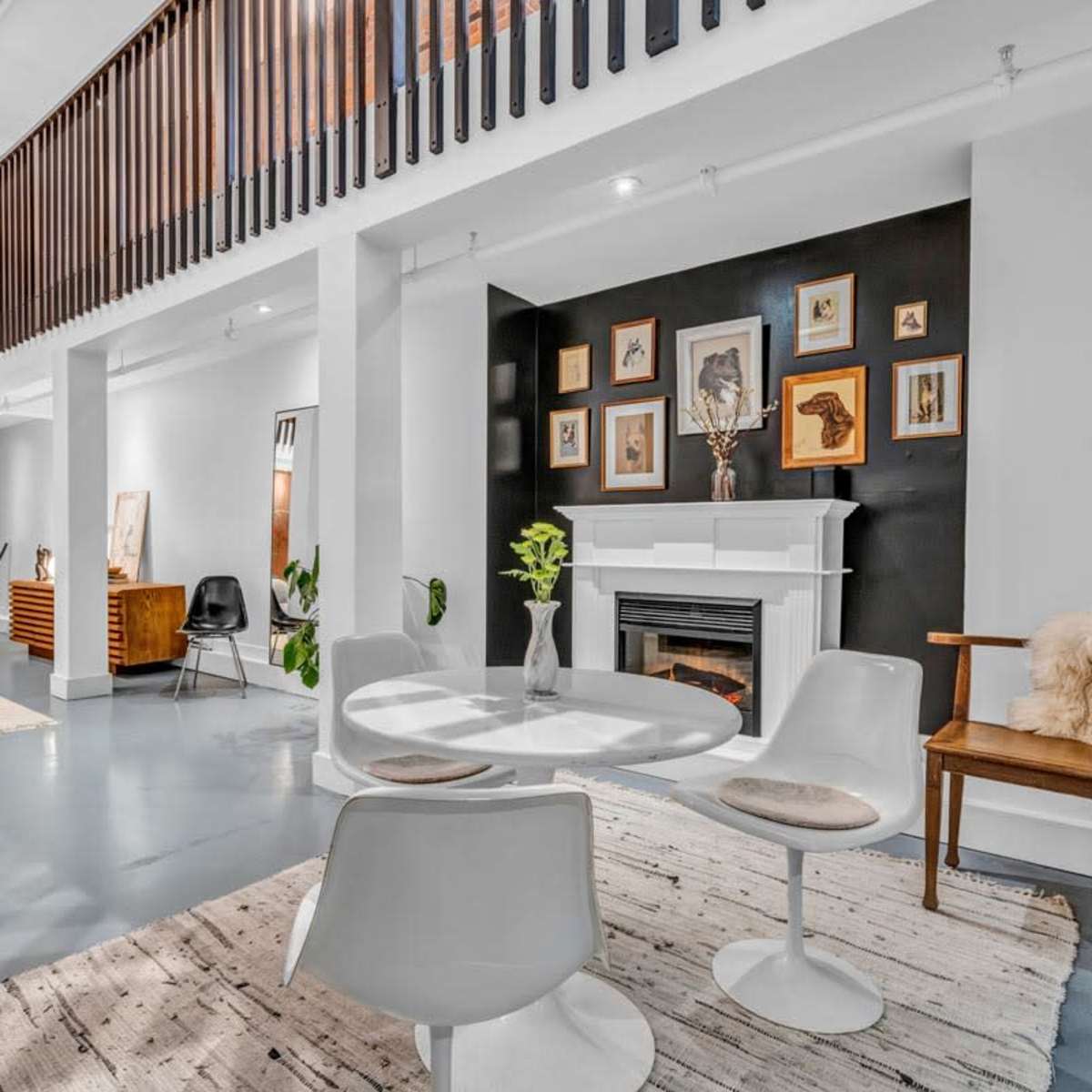 A modern interior features a dining area with a round table and white chairs, surrounded by plants and artwork, alongside a cozy seating area with a fireplace.