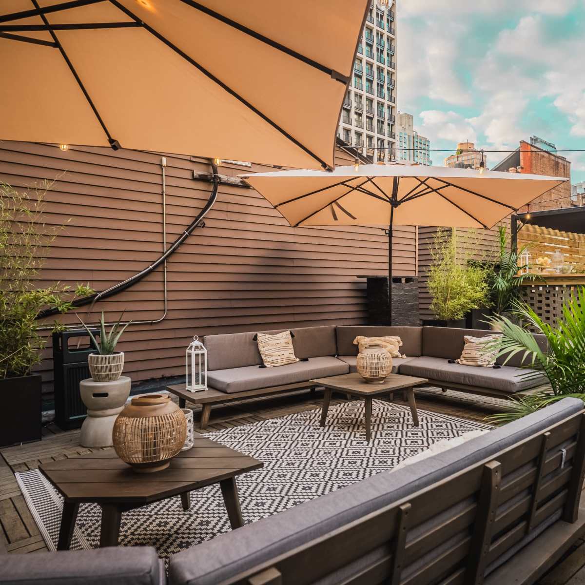A rooftop patio featuring wooden decking, large umbrellas, modern seating arrangements, and greenery.