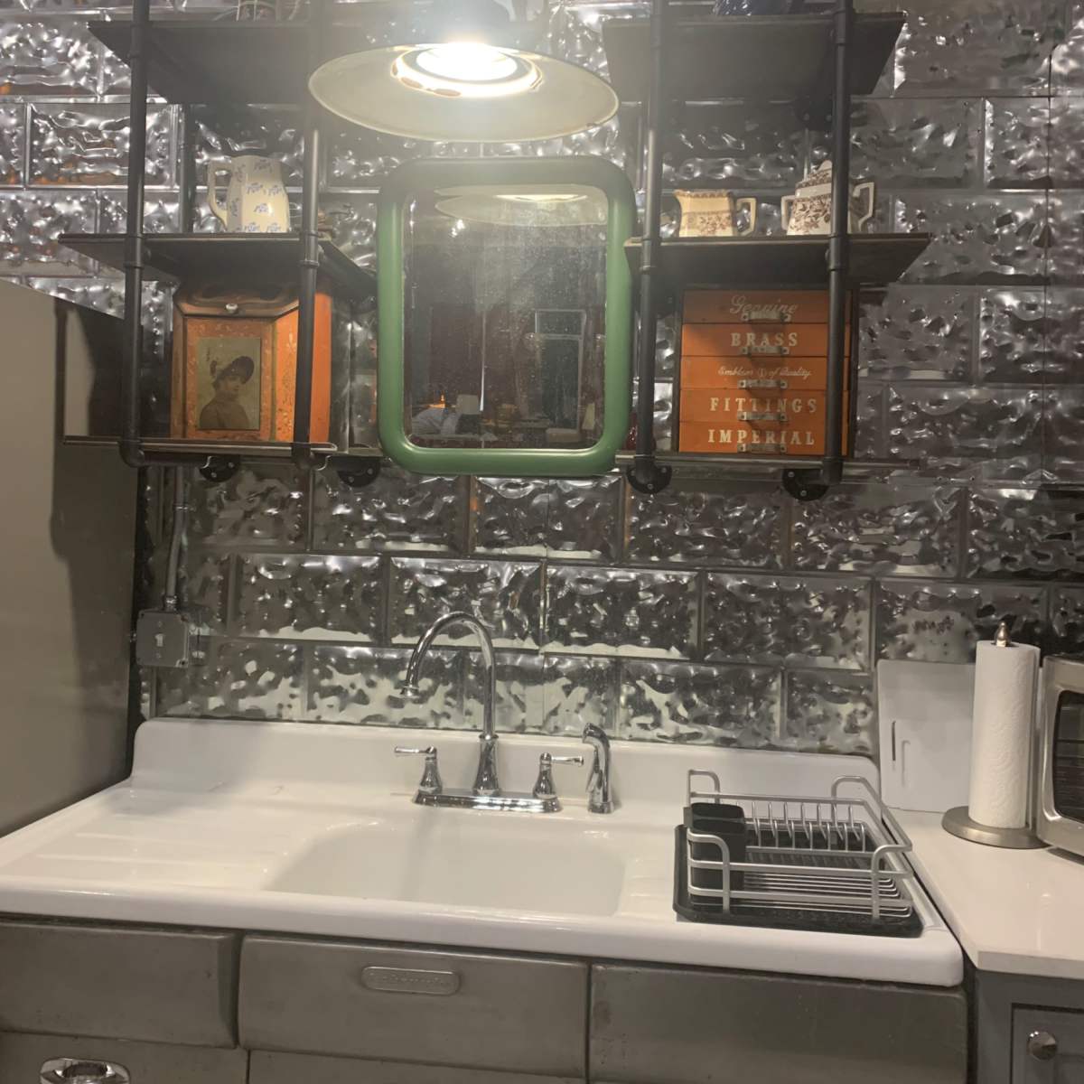 A modern kitchen with a stainless steel sink, shelving unit displaying various items, and a single overhead light.