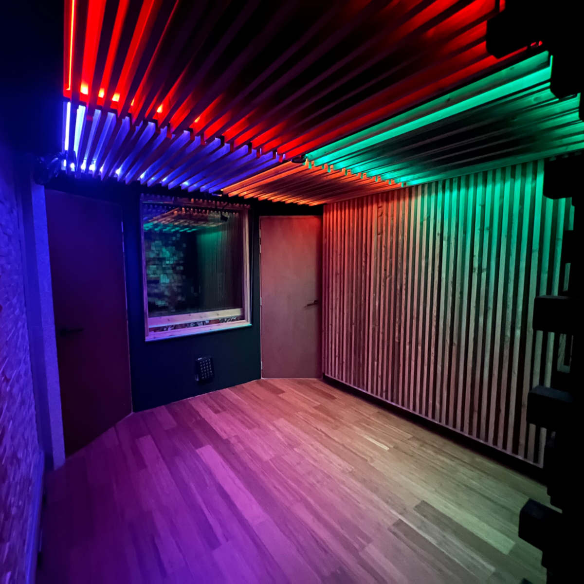 A dimly lit room with colorful LED lights mounted on the ceiling and wooden wall panels.