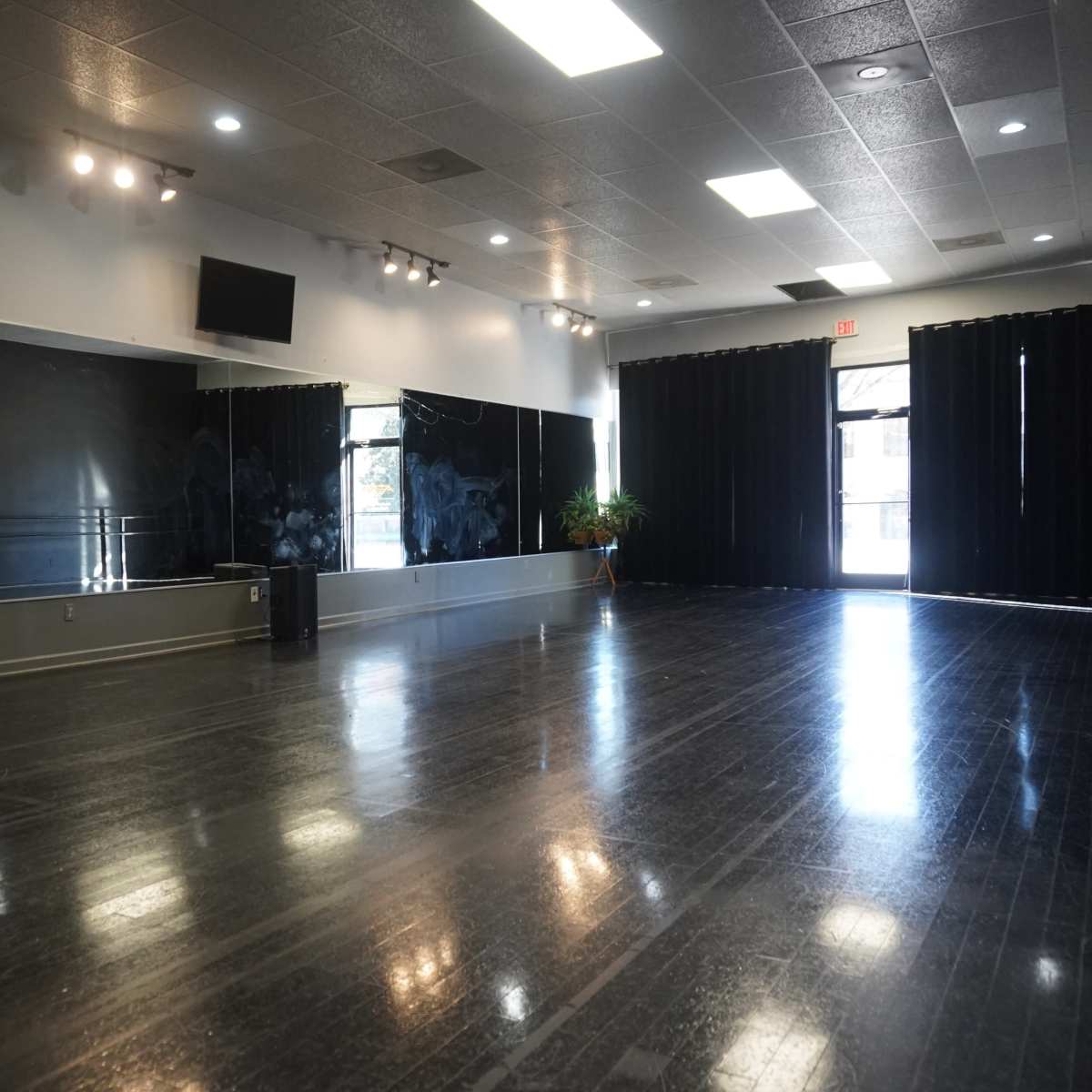 A spacious dance studio with polished wooden floors, mirrors on one wall, and large black curtains along another.
