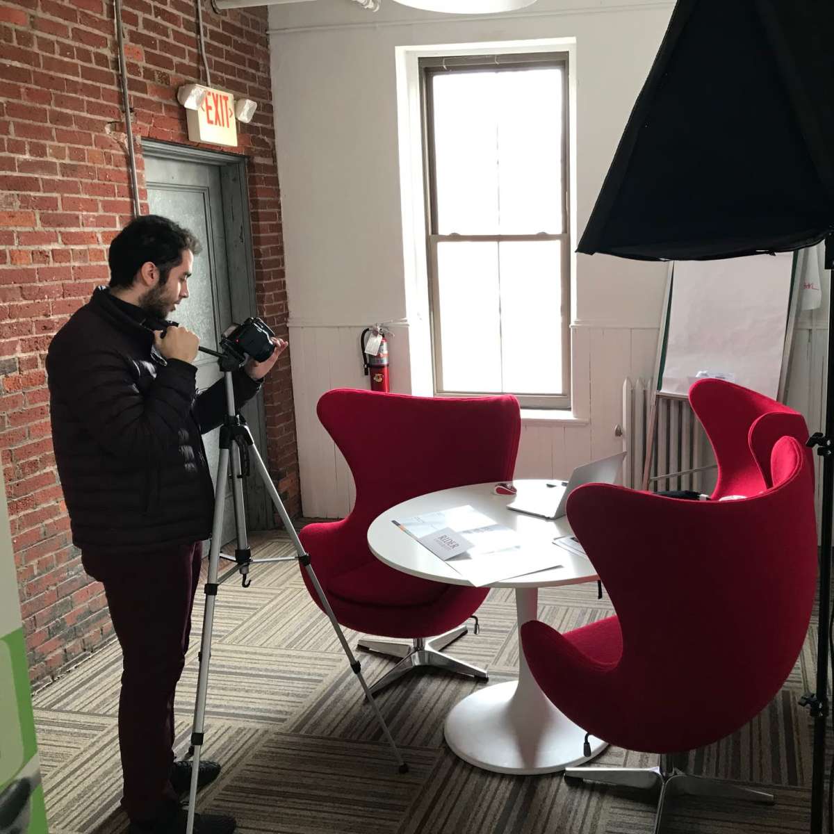 A person is setting up a camera on a tripod in a room with red chairs and a motivational message on the wall.