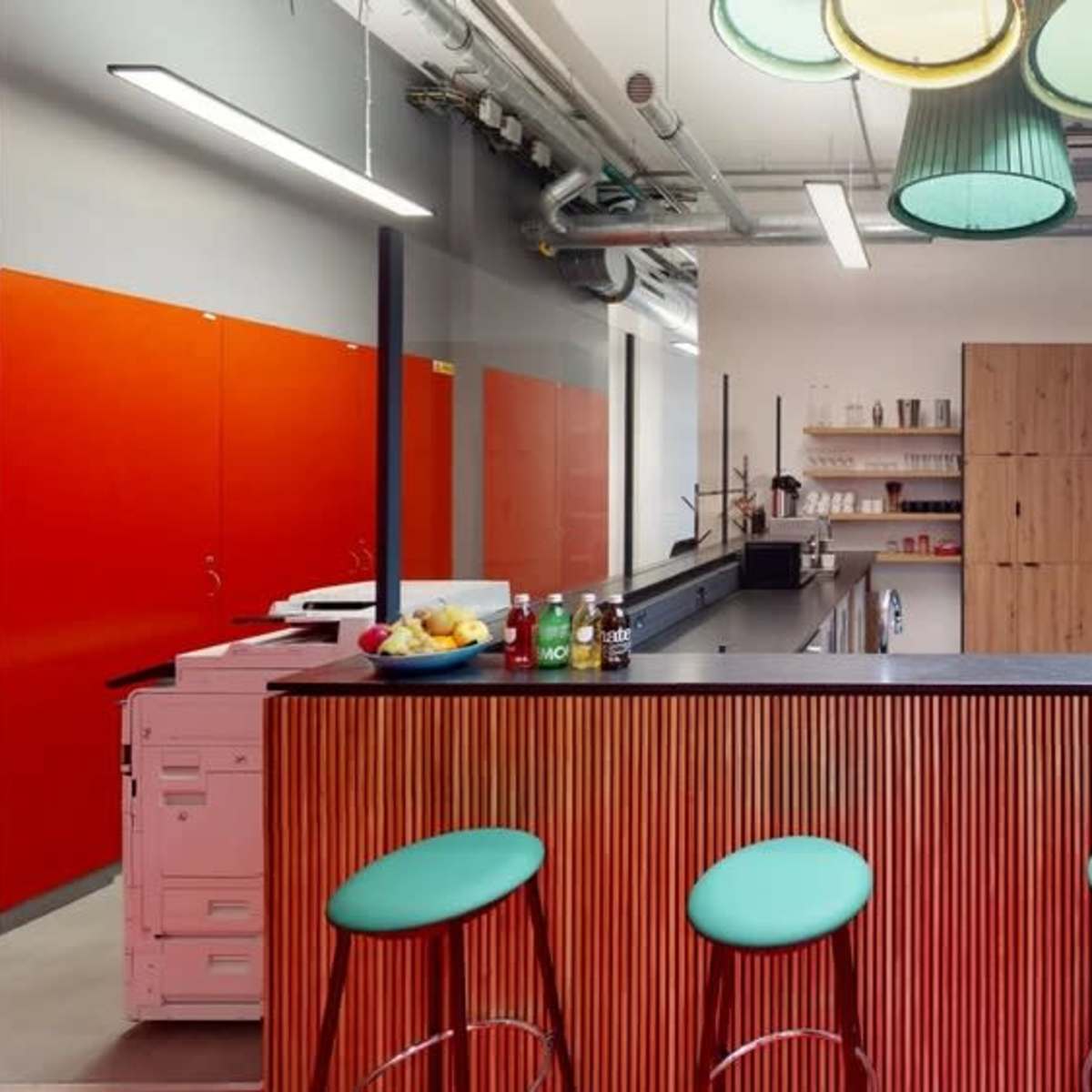 A modern kitchen area with a wooden bar, green stools, orange cabinets, and a black countertop.