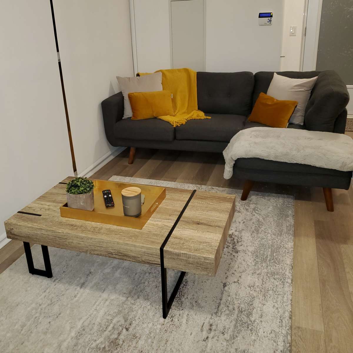 A modern living room with a gray sofa, a wooden coffee table, and a light-colored rug.