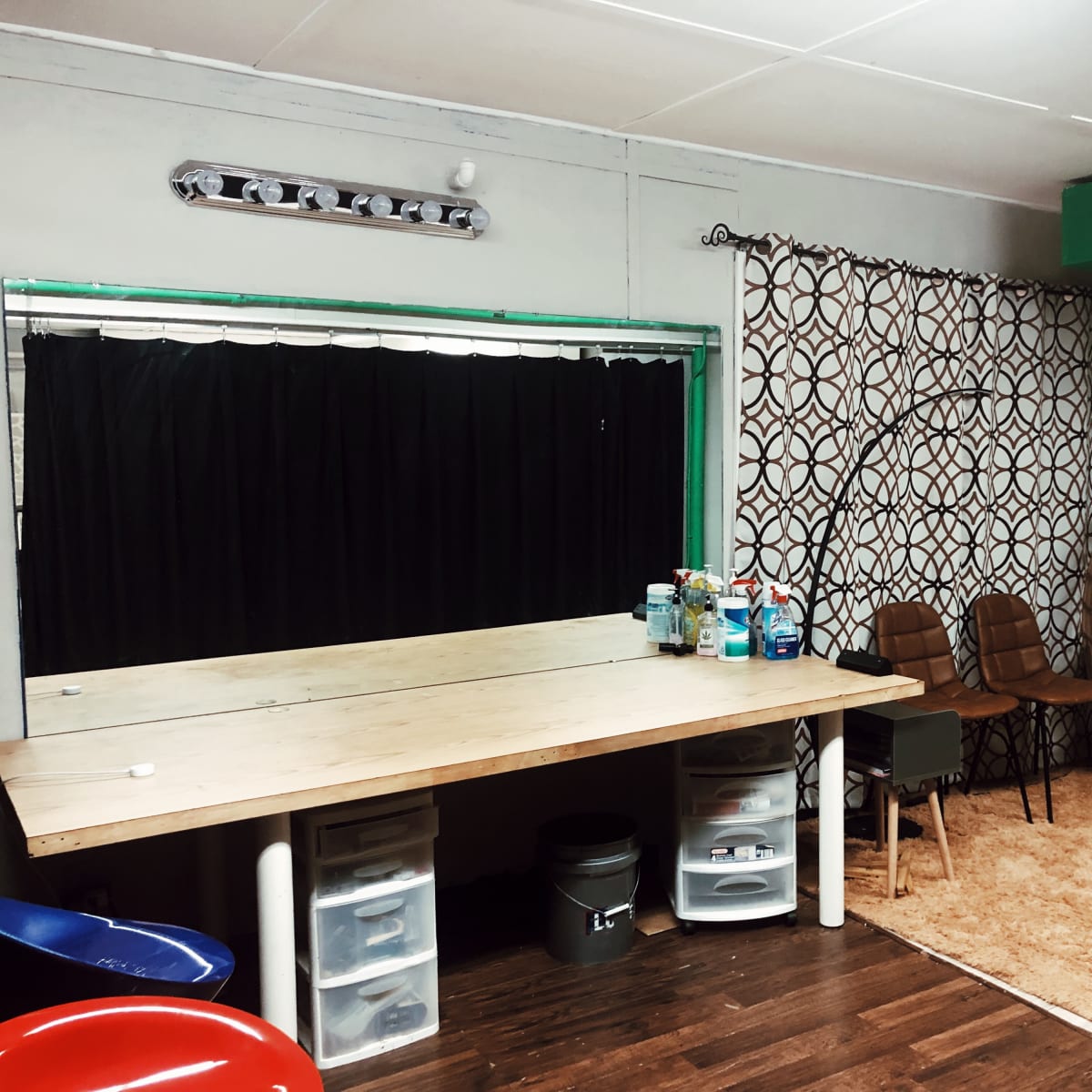 A room with a large wooden table, several plastic containers, two chairs, a hanging chair, and patterned curtains in a neutral color scheme.