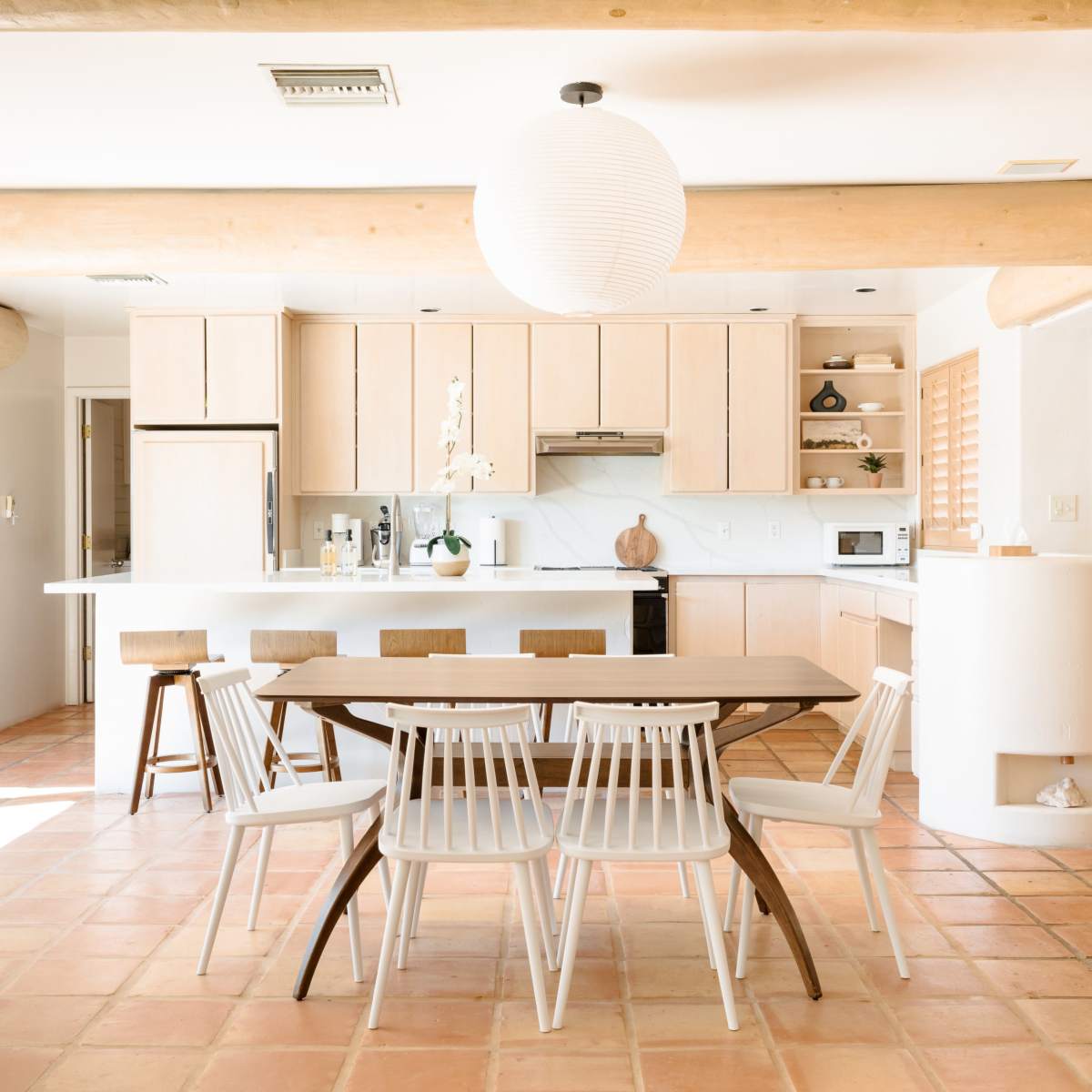 A modern kitchen features light wood cabinetry, a round wooden dining table surrounded by white chairs, and a pendant light illuminating the space.