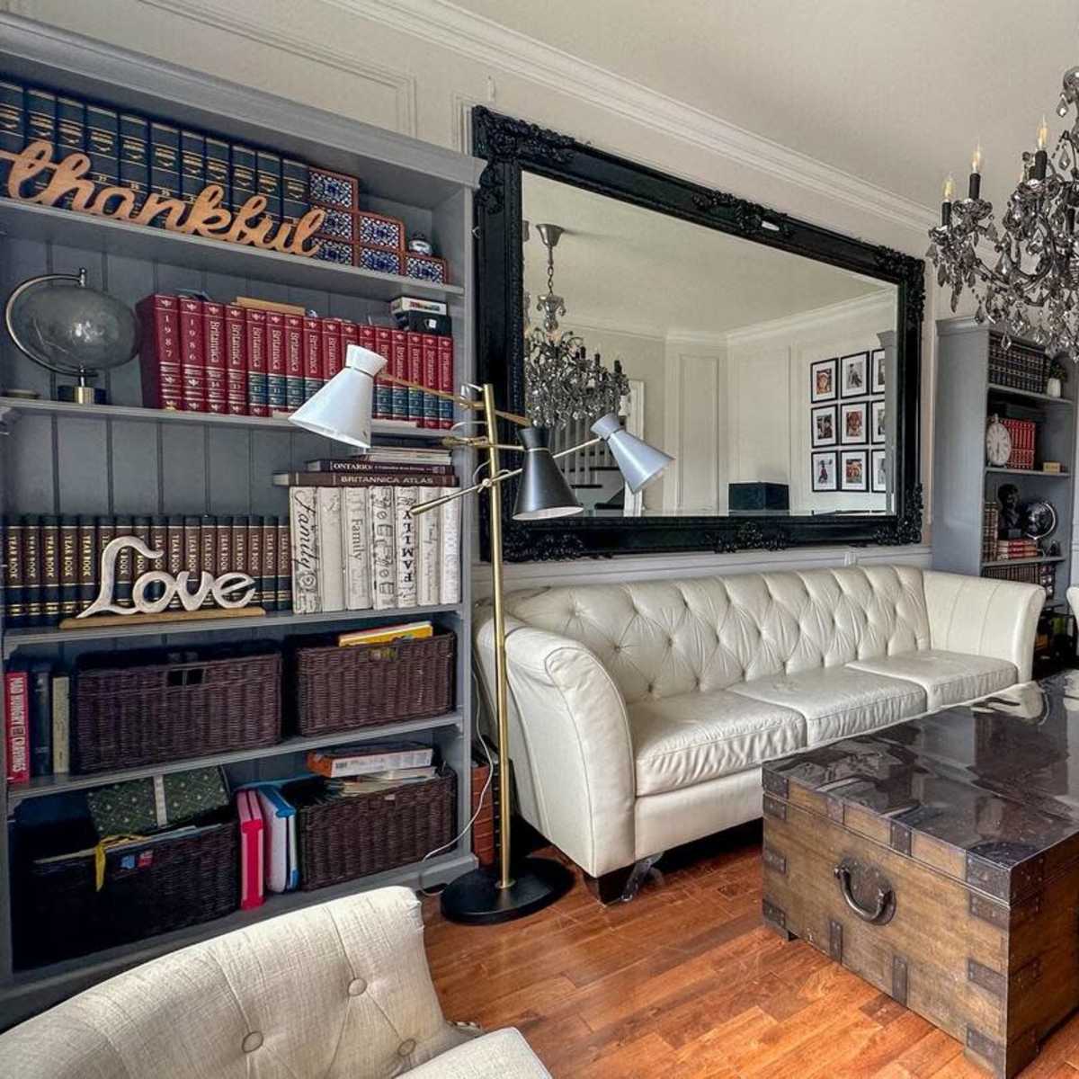 A well-furnished living room with two white leather sofas facing a wooden coffee table, surrounded by bookshelves and framed photographs.
