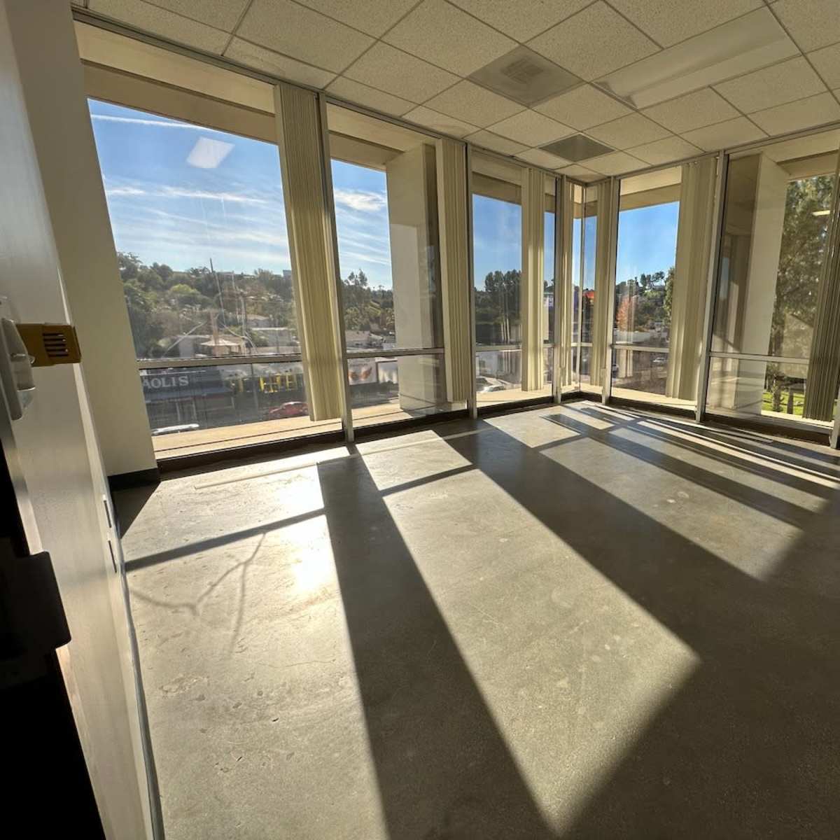 An empty office space with large windows that allow sunlight to cast shadows on the floor.