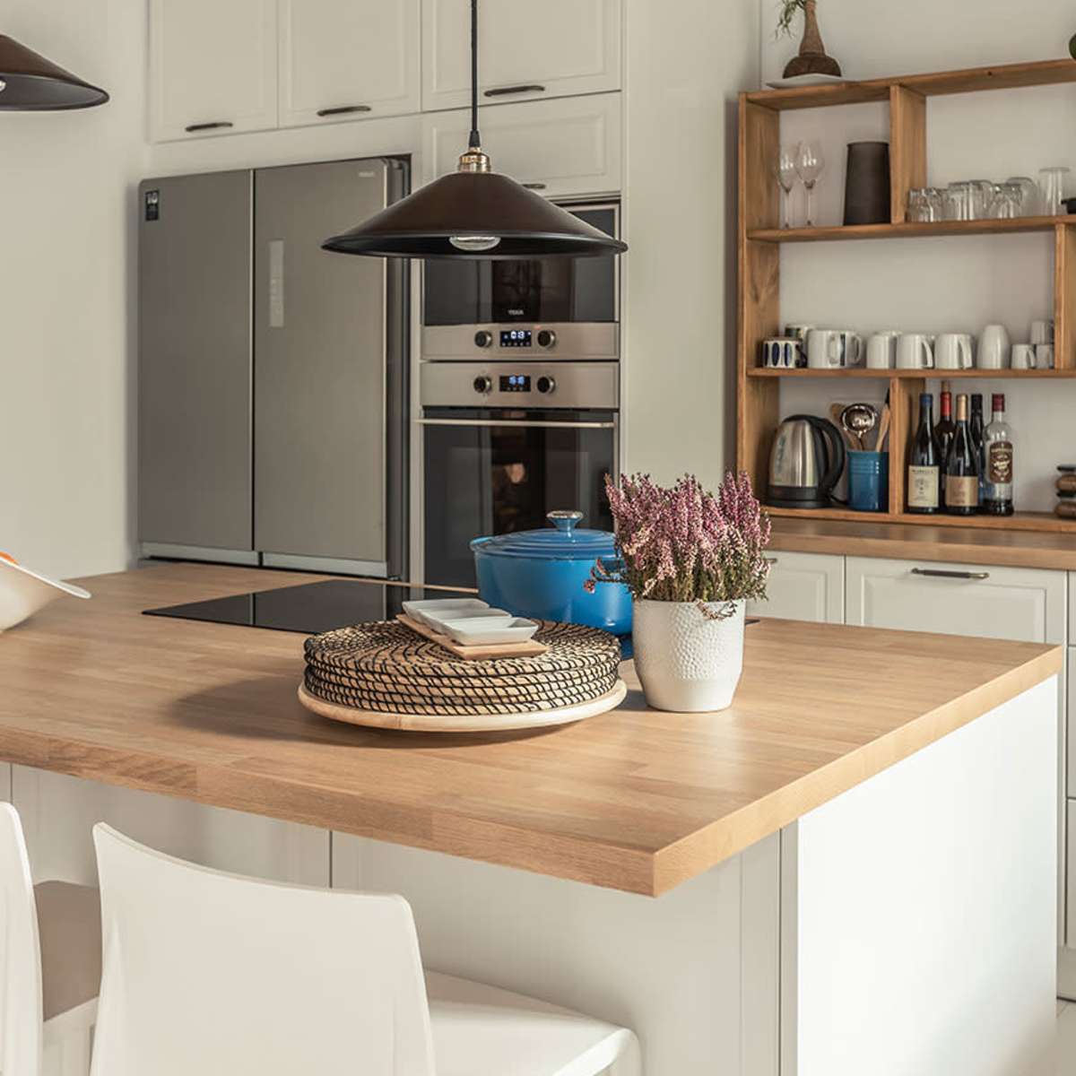 A modern kitchen features a wooden island with a basket and a potted plant, surrounded by appliances and neatly organized shelves.
