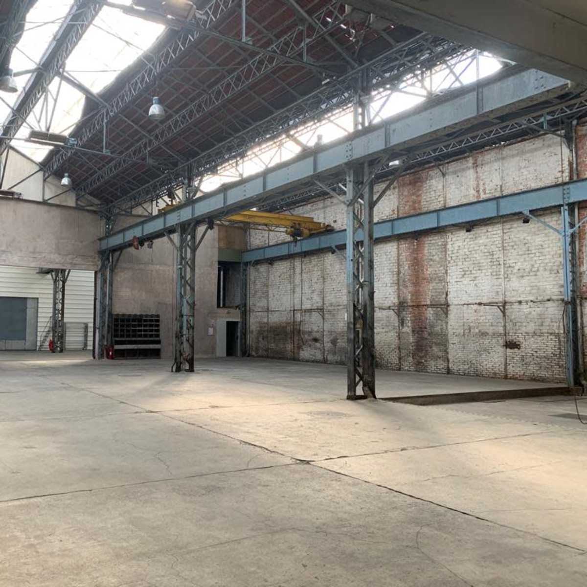 An empty industrial warehouse features high ceilings, exposed beams, and concrete floors.