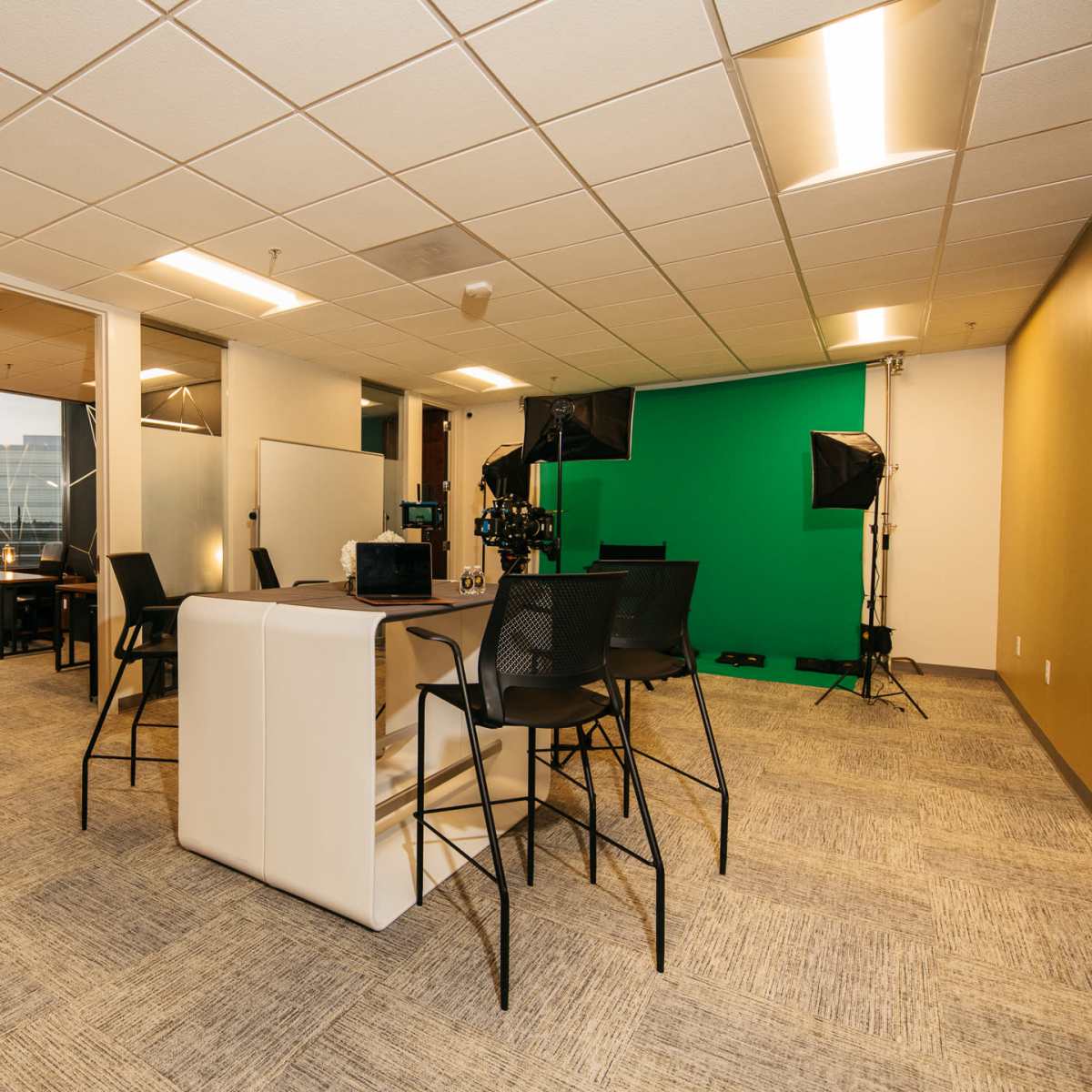 A modern workspace with a green screen setup, several cameras, a large table for meetings, and seating arrangements.