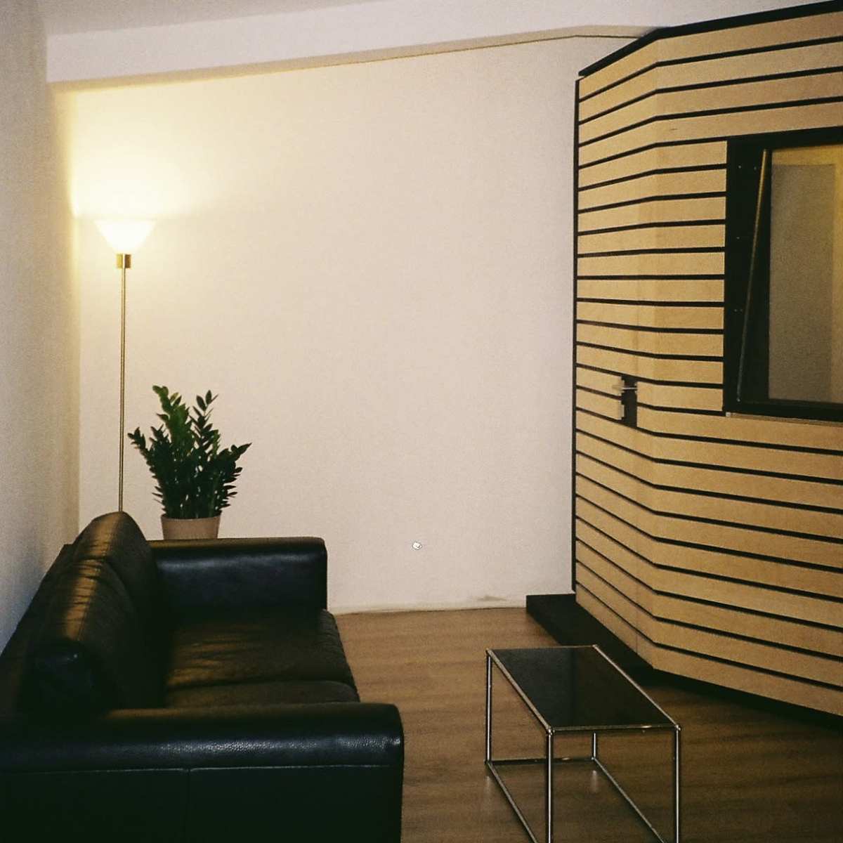 A modern interior space featuring a black leather sofa, a coffee table, and a partitioned area with striped walls and a mirror.