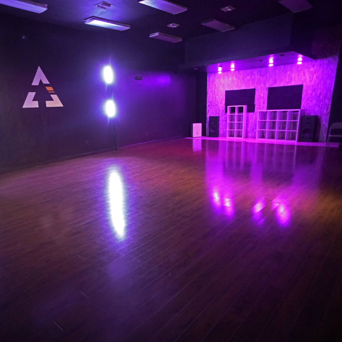 A dance studio with polished wooden floors, purple lighting, and a minimalist design featuring a geometric logo on the wall.