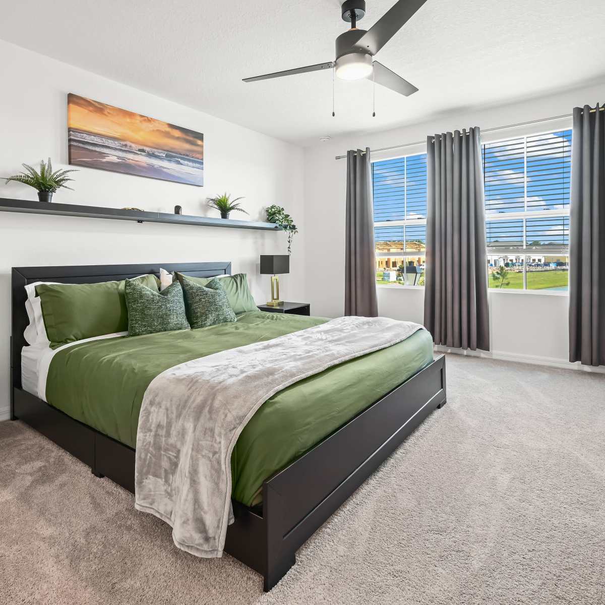 A well-styled bedroom features a black bed with green bedding, a nightstand, and a large window with sheer curtains, allowing natural light to illuminate the space.