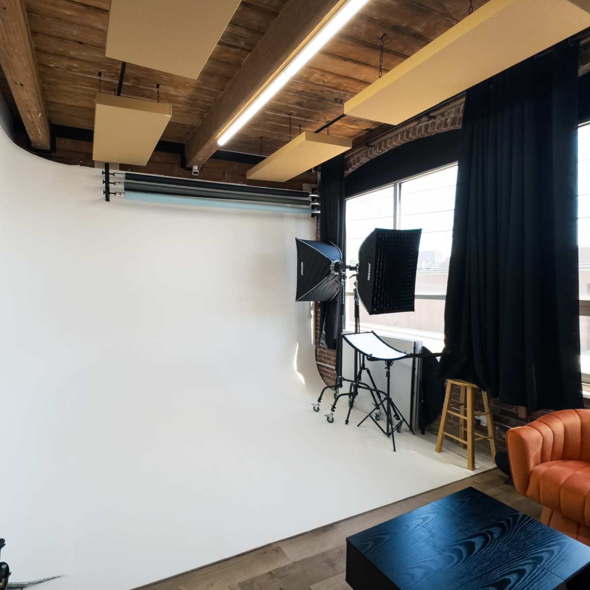 A photography studio with a large white backdrop, lighting equipment, and wooden ceiling beams.