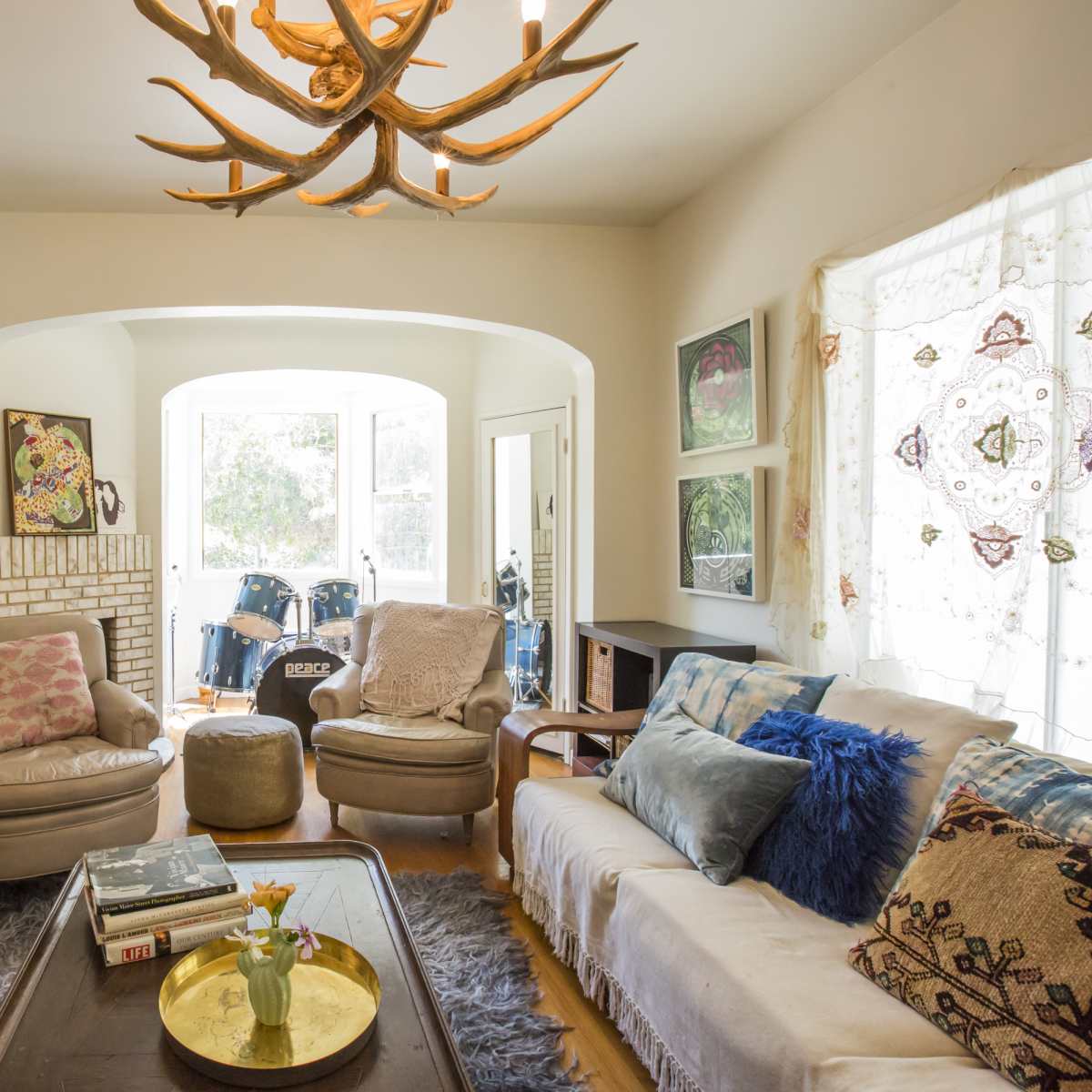 A cozy living room features a large window, comfortable seating, and a decorative antler chandelier.