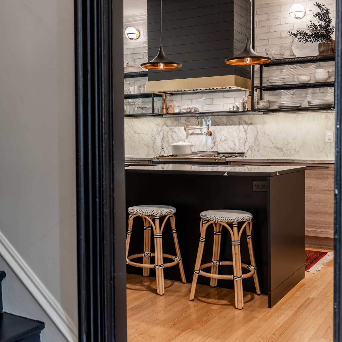 A modern kitchen with a marble countertop, two bar stools, and pendant lights above an island.