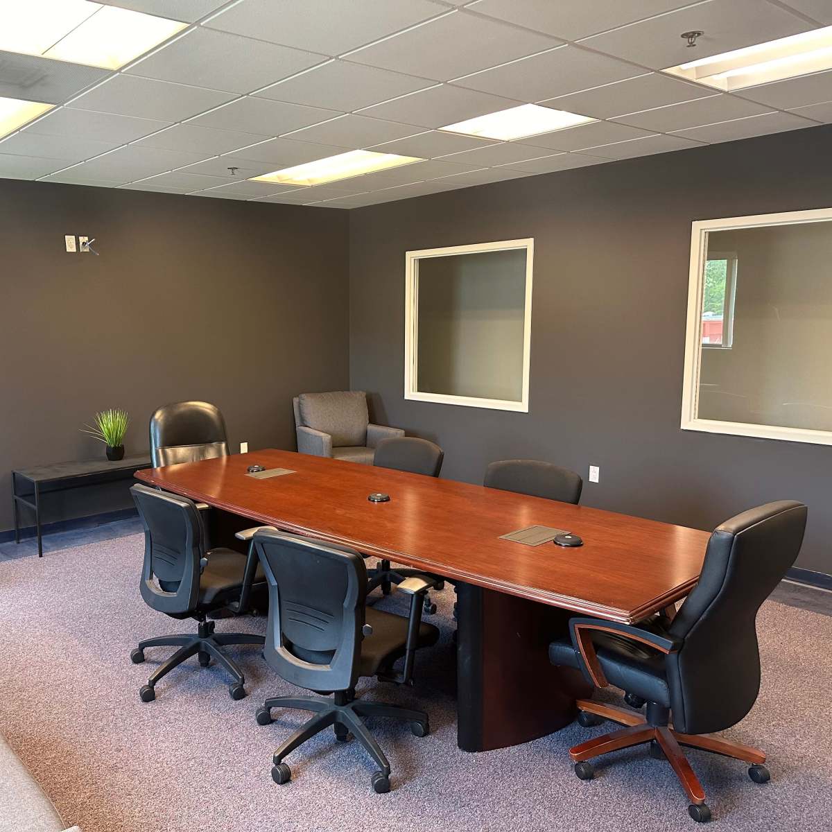 A conference room with a large wooden table surrounded by black chairs and a small seating area with gray sofas.