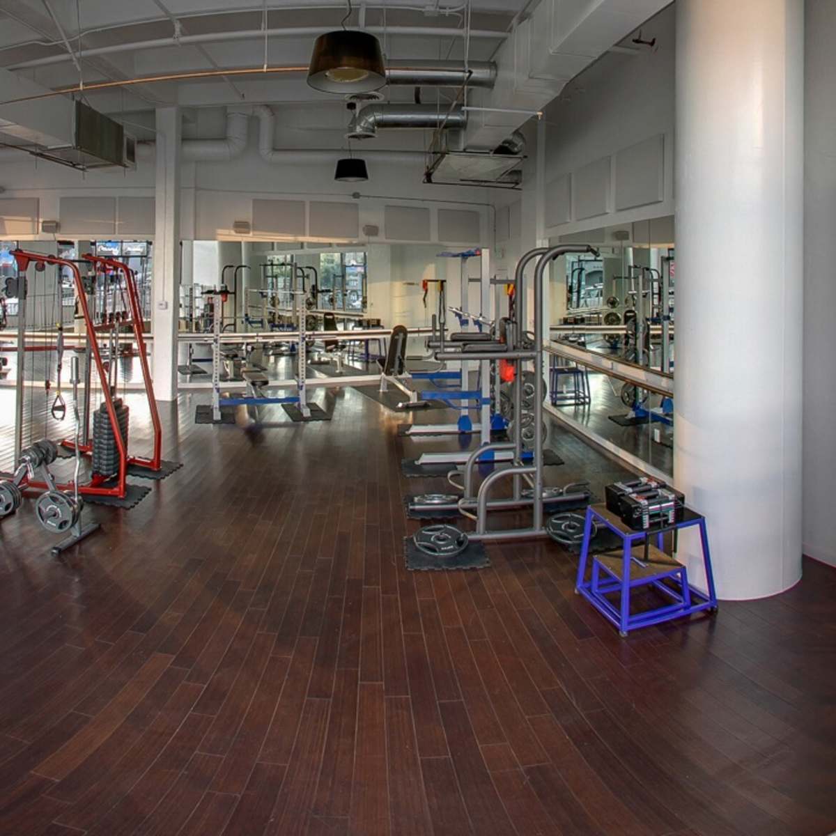 A spacious gym interior with various exercise equipment arranged on polished wooden floors.