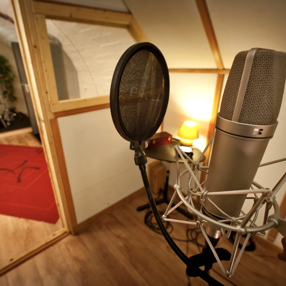 A microphone stands in the foreground with a soundproof booth and a drum set visible in the background.