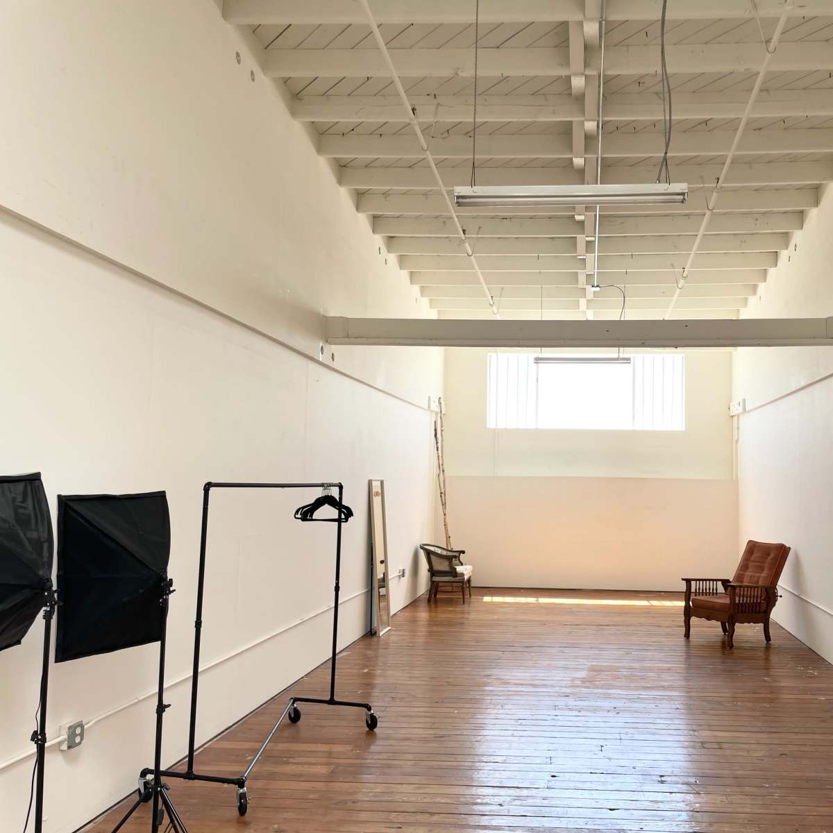 A spacious, empty room with wooden flooring, tall white walls, and a single vintage armchair at one end.