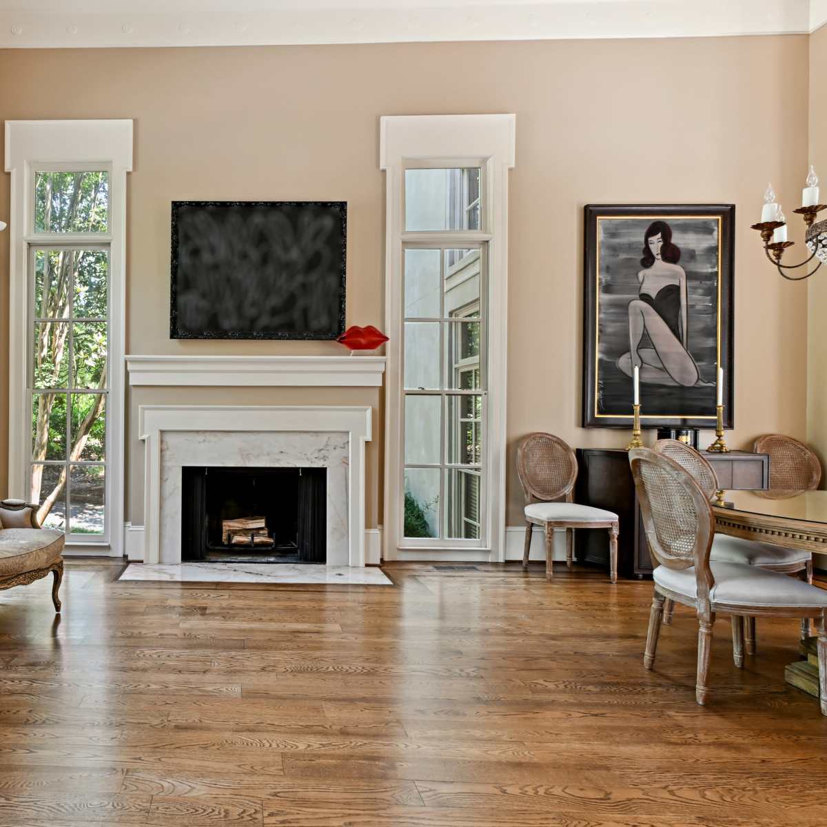A well-lit living room features a fireplace, large windows, and elegant furniture arranged around a central space.