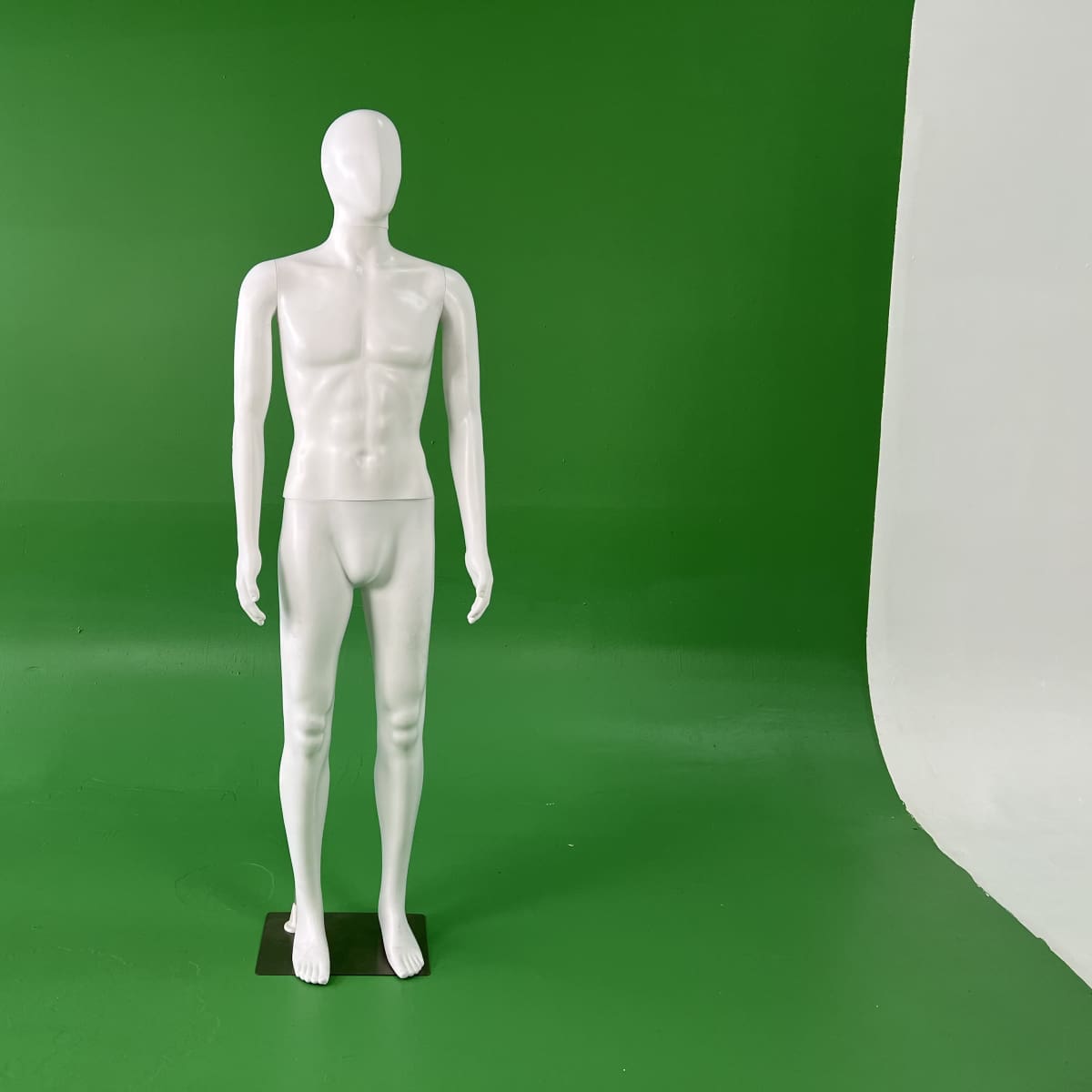 A white mannequin stands upright on a black base in front of a green backdrop.