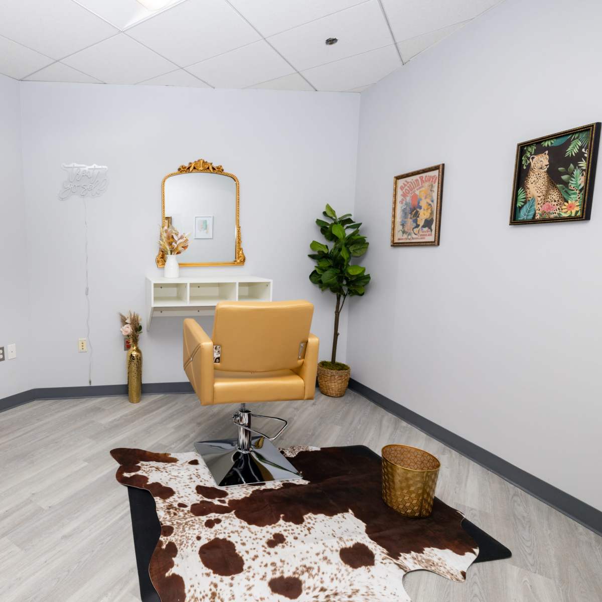 A minimalist salon room featuring a yellow styling chair, a wall-mounted mirror, and decorative art pieces.