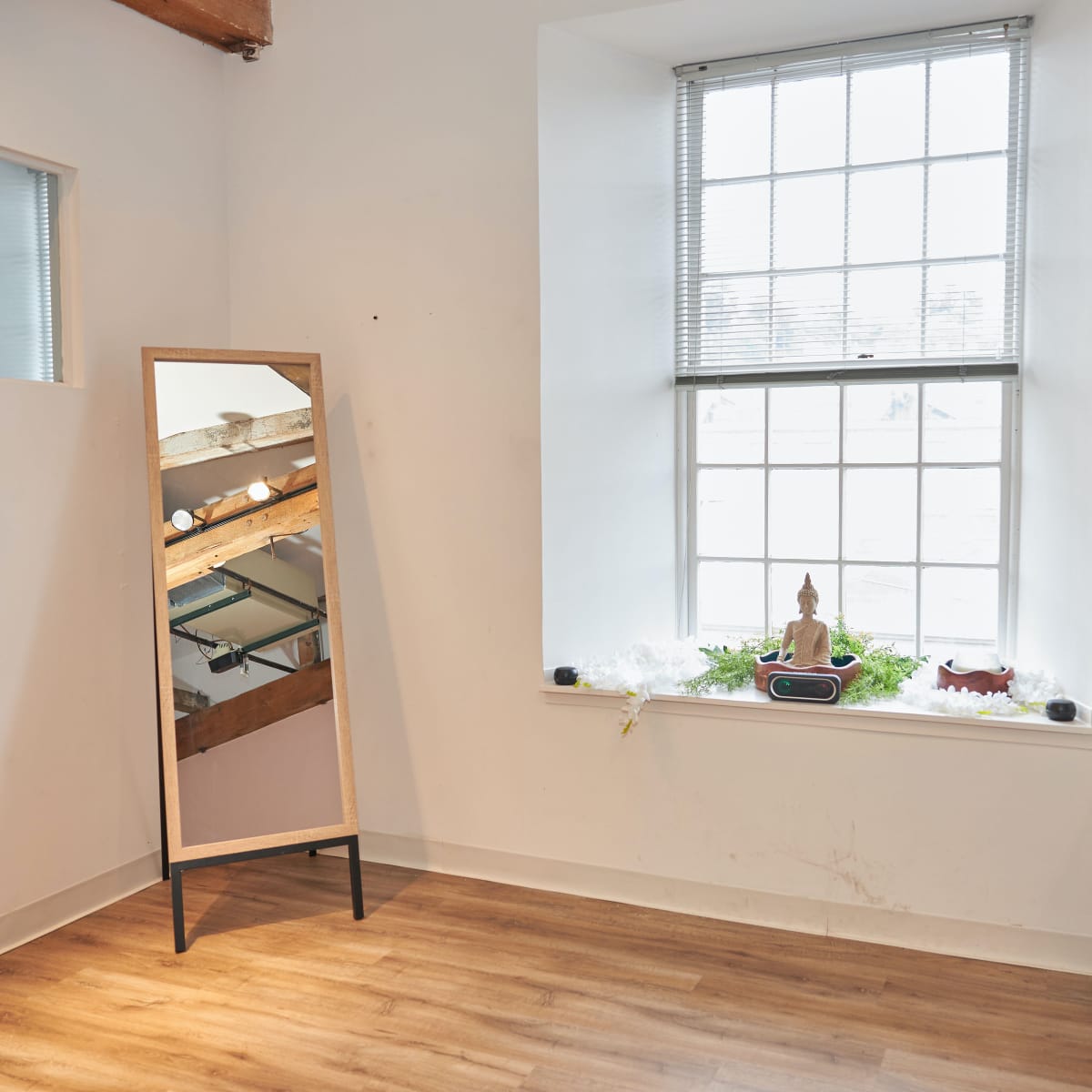 A large mirror leans against the wall beside a windowsill adorned with decorative items, including a small statue.