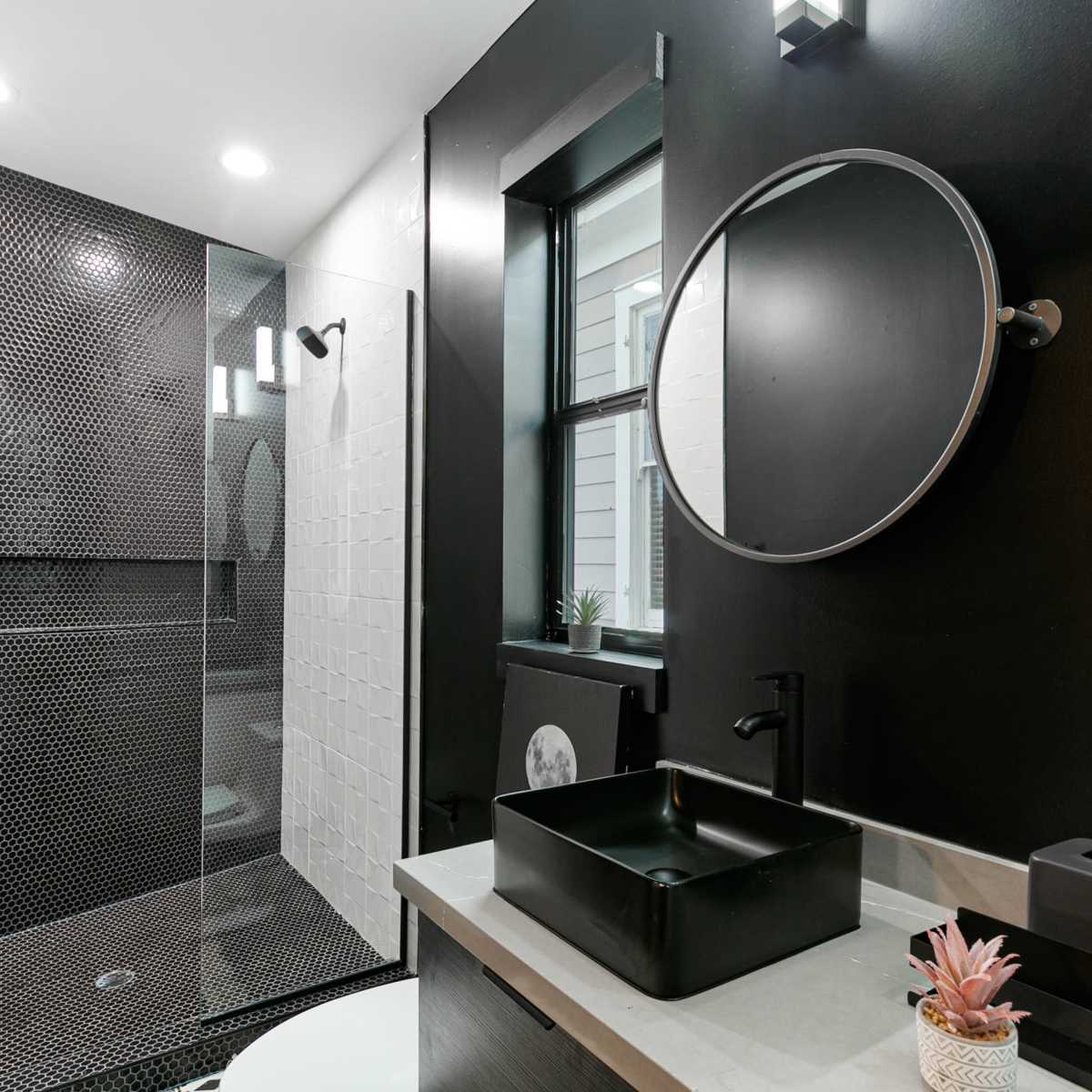 A modern bathroom featuring a black and white color scheme, with a glass shower, circular mirrors, and a sleek sink.
