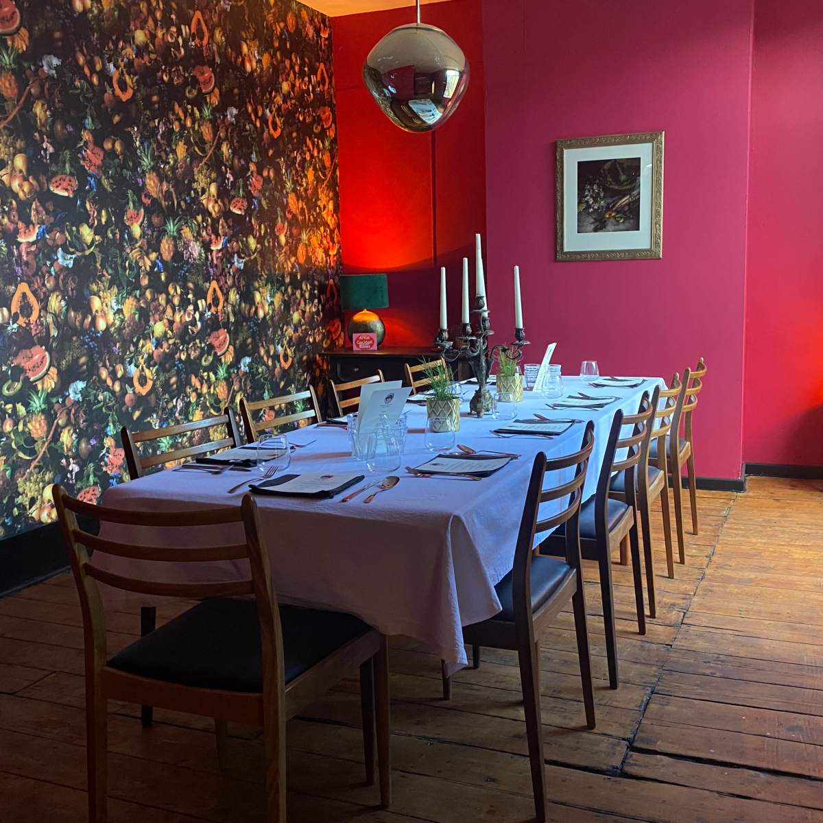 A long dining table is set for a meal in a brightly colored room with floral wallpaper and a large disco ball.