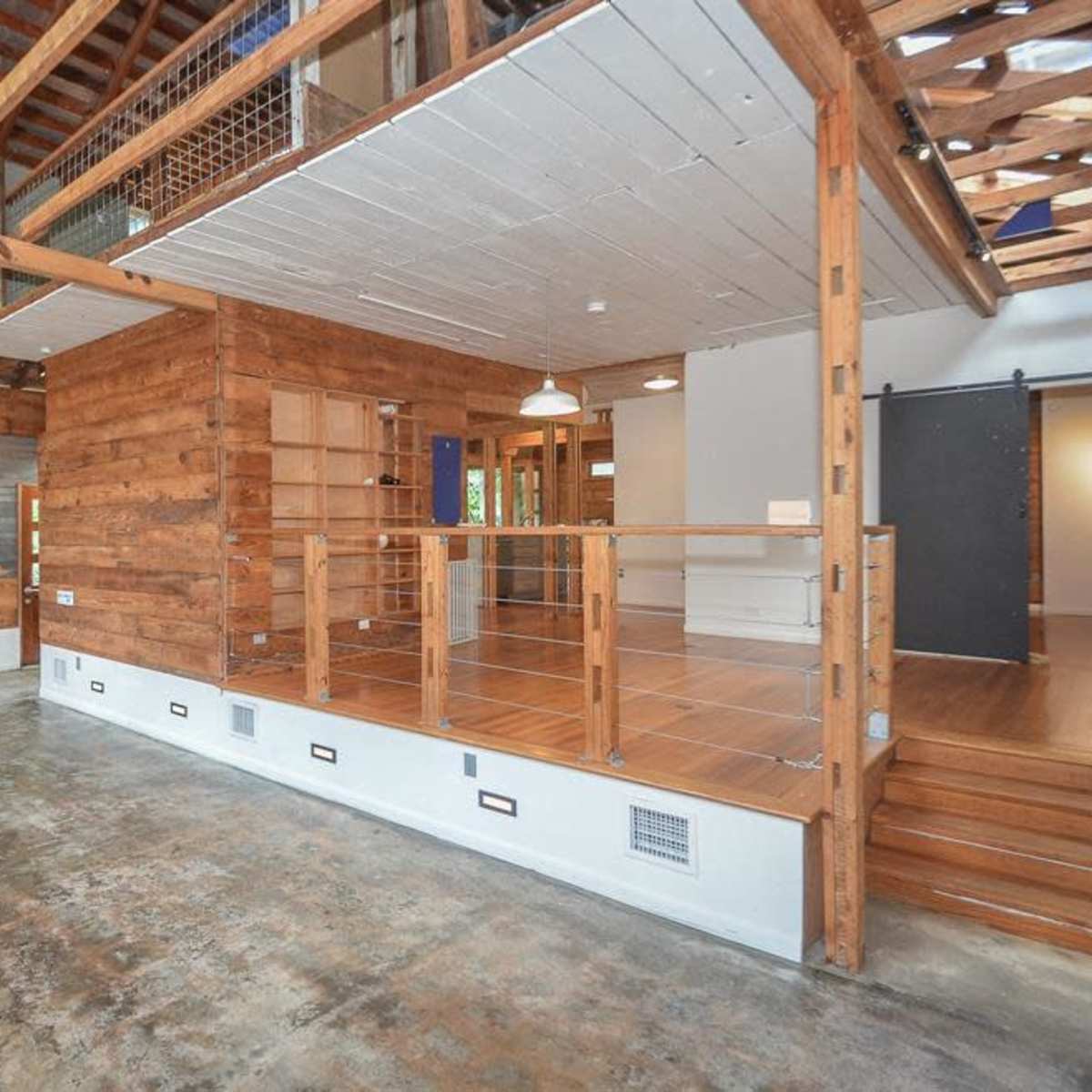 An open-concept room with wooden walls, exposed beams, and a concrete floor.