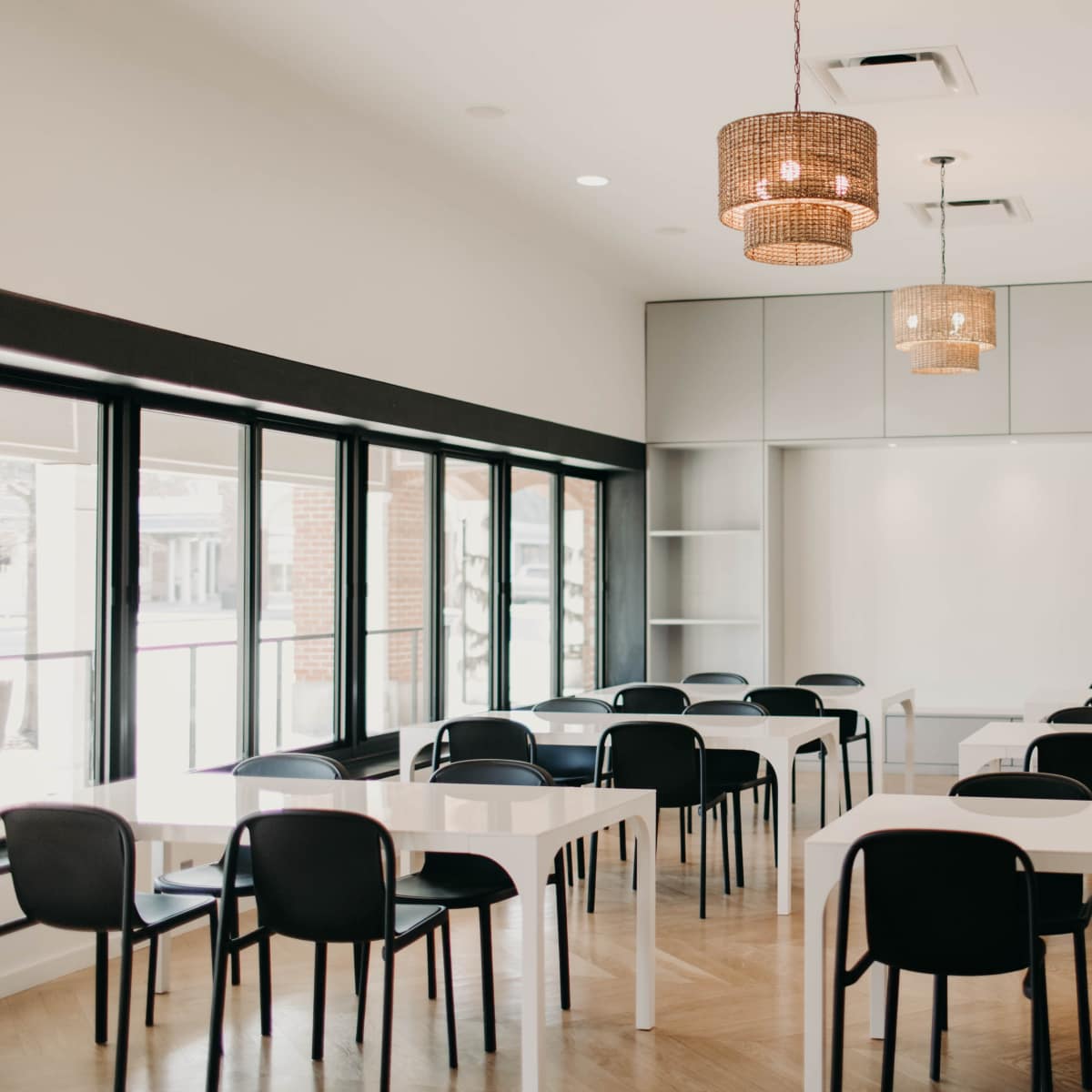 A bright conference room features multiple rectangular tables and black chairs, with large windows allowing natural light to illuminate the space.