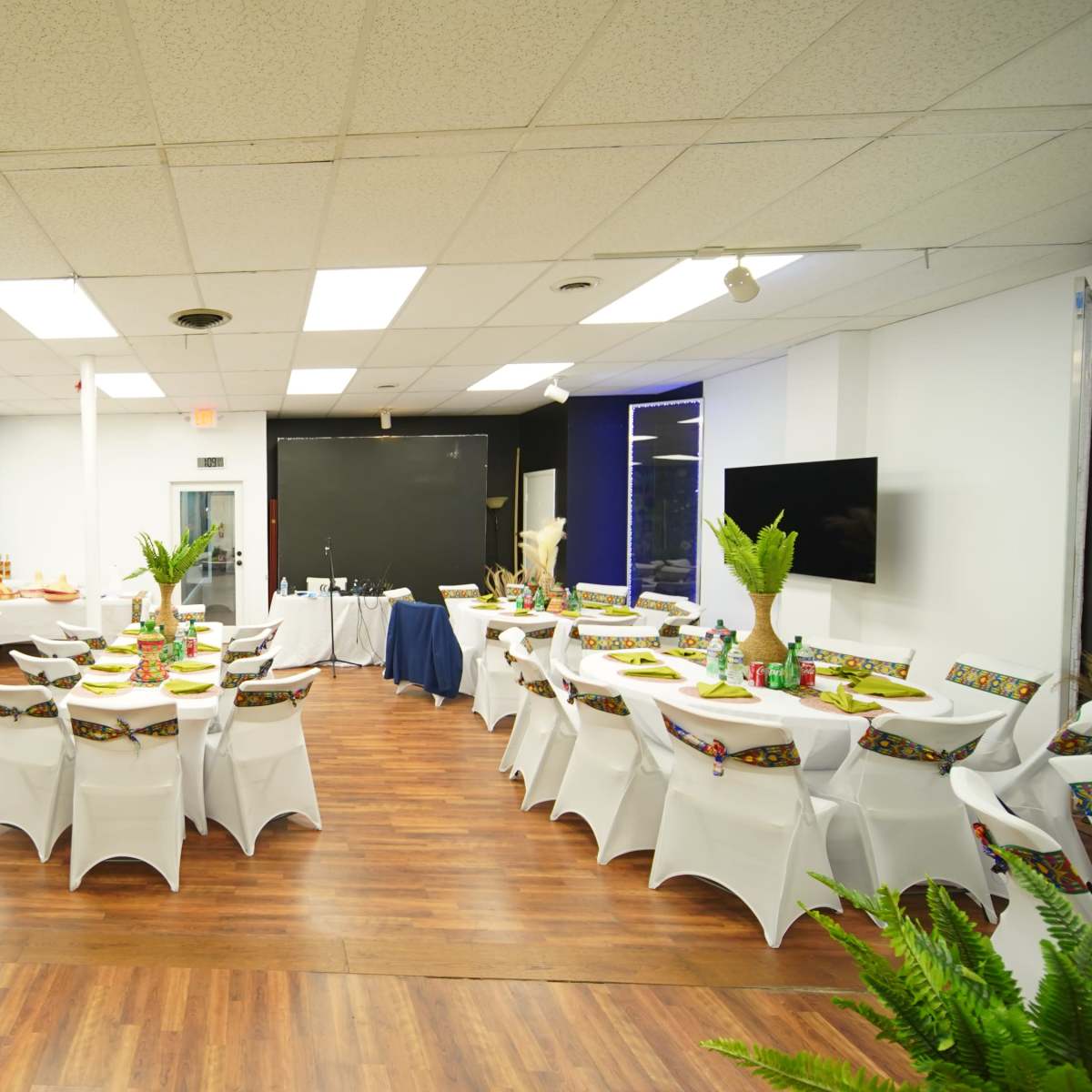 A banquet hall arranged with round tables covered in white tablecloths, decorated with centerpieces and seating for guests.