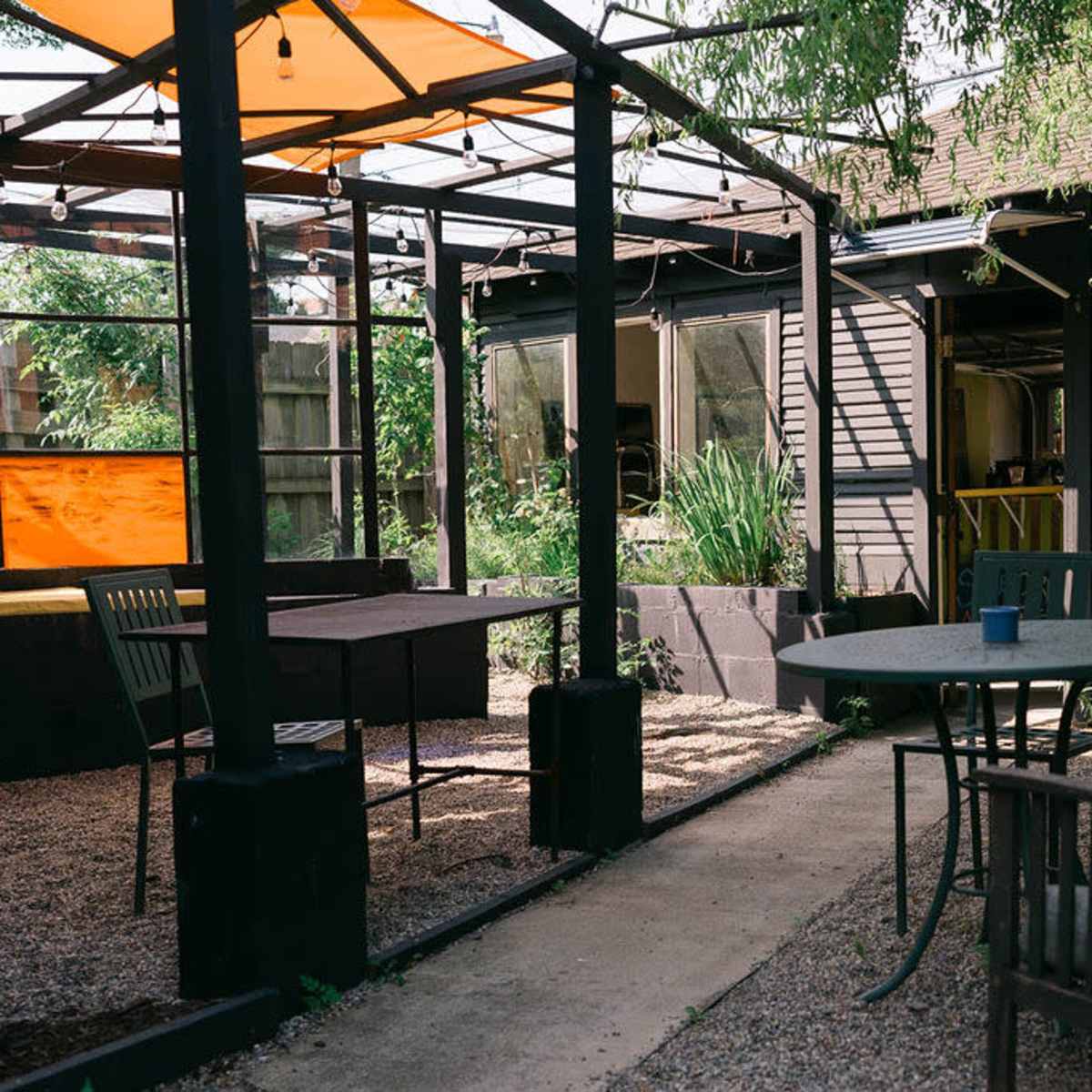 A garden area with several tables and chairs surrounded by greenery and a structure with a glass roof.