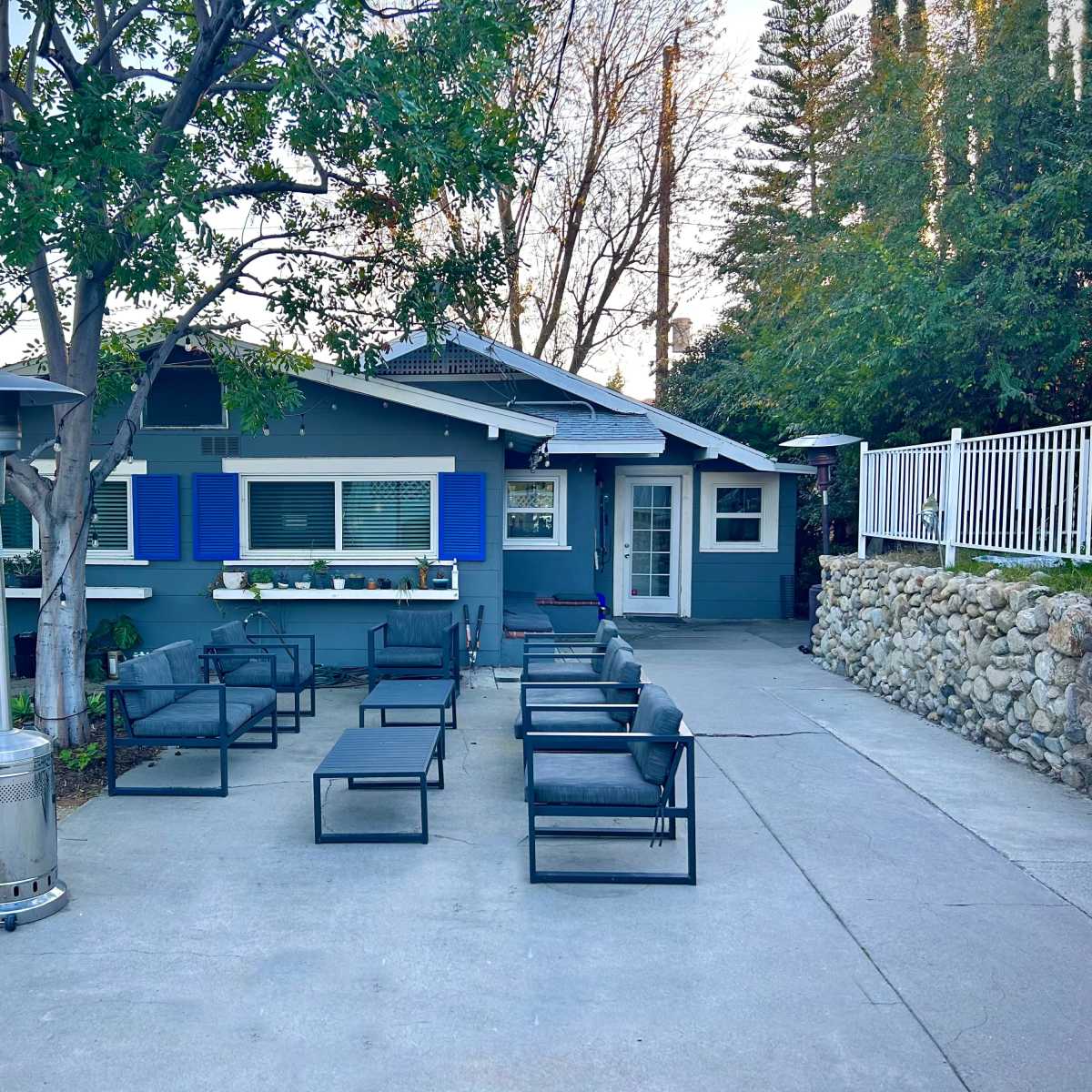 A blue-trimmed house with a patio area is surrounded by seating and landscaping features.