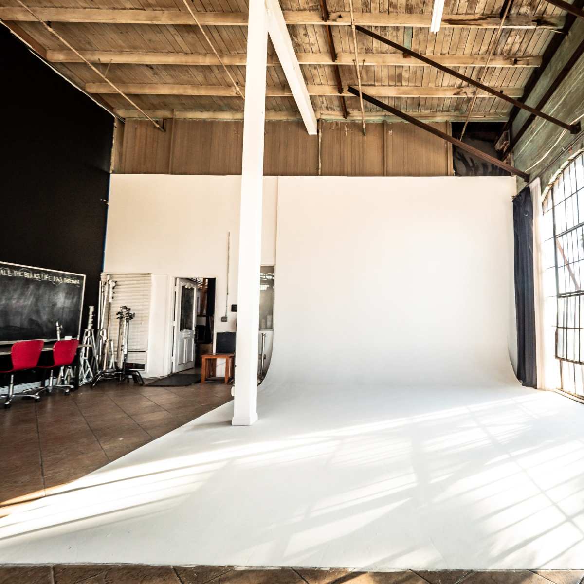 A spacious photography studio with a white backdrop, large windows, and exposed wooden beams.