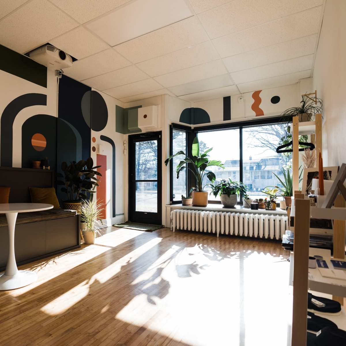 A modern interior space with a patterned mural on the wall, a round table, seating area, and large windows allowing natural light to enter.