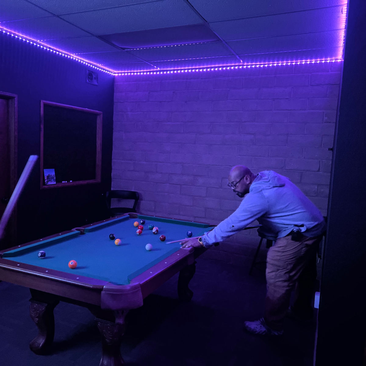A dimly lit room features a pool table with colorful balls, while two individuals are engaged in a game.