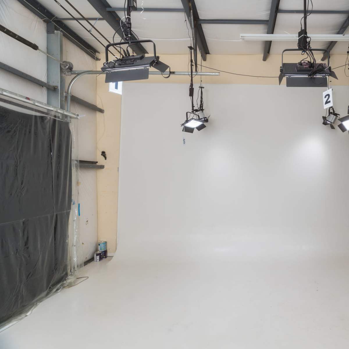 A blank photographic studio with a seamless white backdrop and several ceiling-mounted lights.