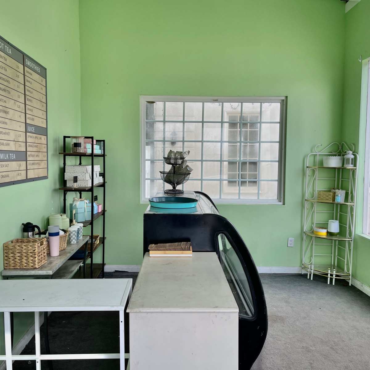 A minimalist café interior with a green wall, a display counter, menu board, and various shelves filled with products.