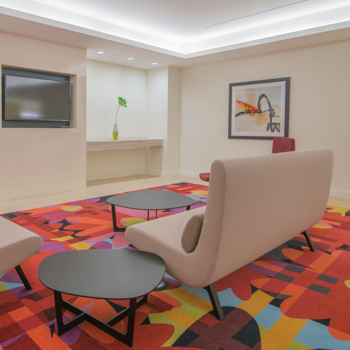 A modern lounge area featuring two upholstered chairs, a low black coffee table, and a colorful area rug in a brightly lit room.