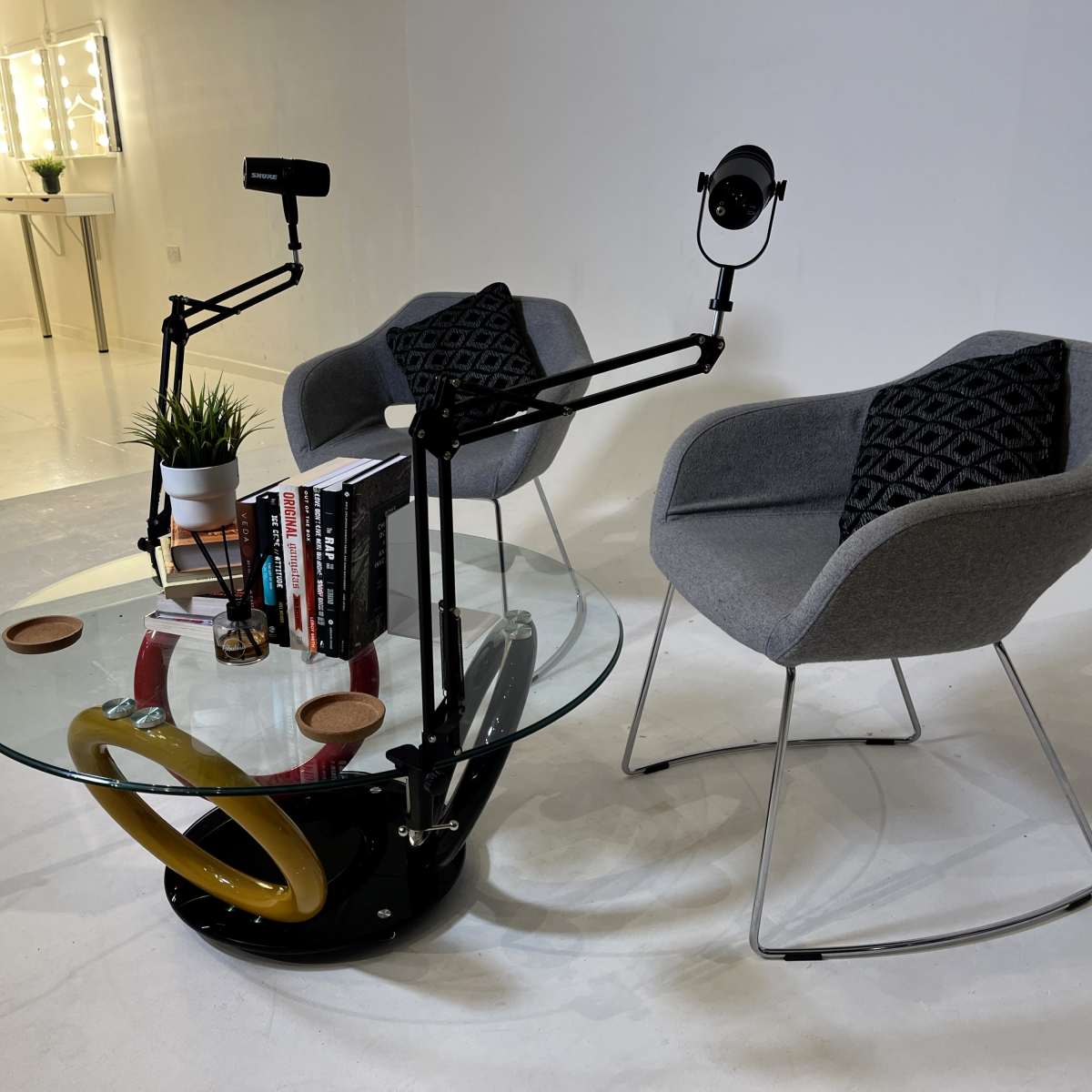 A modern setup with two gray chairs, a circular glass coffee table, and a few books, all positioned in a minimalist indoor space.