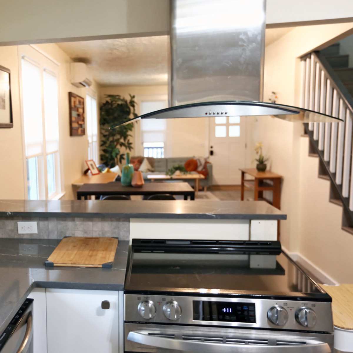A modern kitchen with stainless steel appliances, a countertop, and open shelving displaying glassware, leading into a dining area in the background.