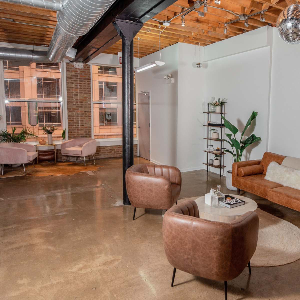 A modern, open-concept living space featuring a brown leather sofa, two leather chairs, a round coffee table, and large windows illuminating the room.