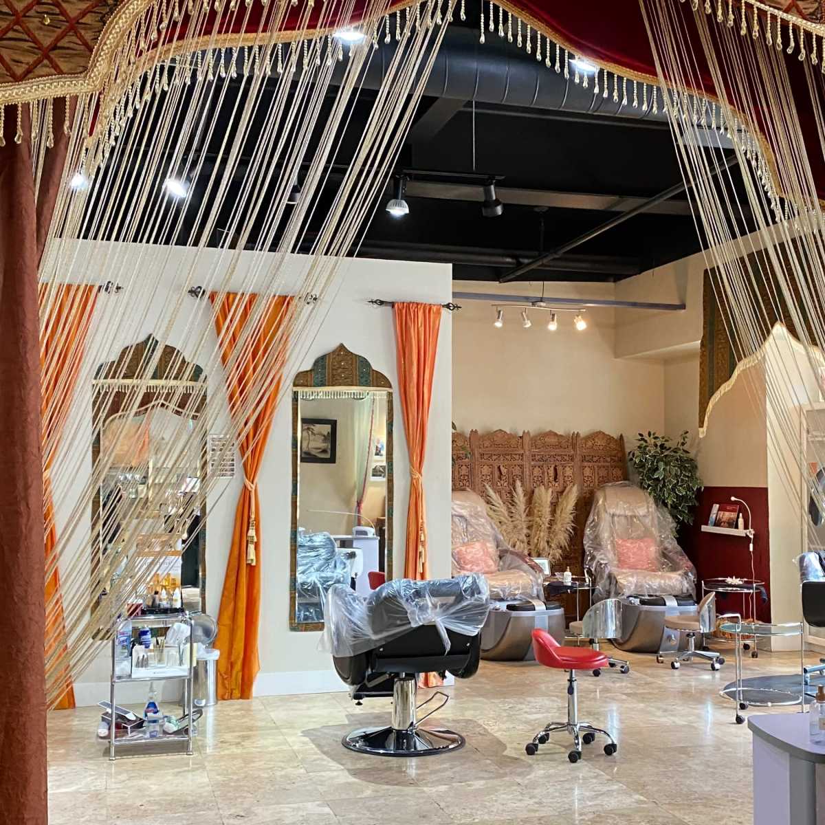 A salon interior features hair styling stations separated by decorative fabric drapes, with a warm color palette and ornate walls.