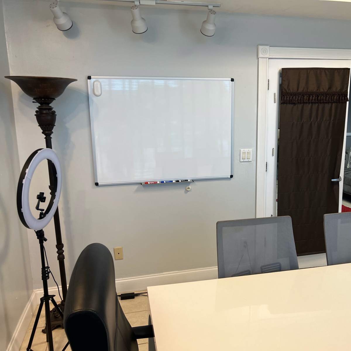 A meeting room with a whiteboard on the wall, a large table with chairs, and a ring light placed beside a floor lamp.