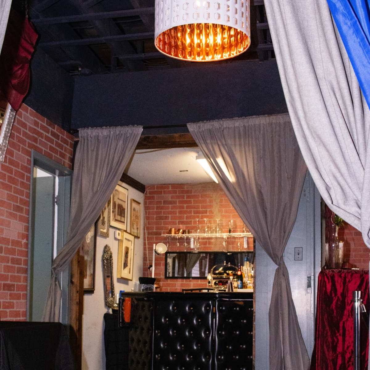 A stylish interior featuring a bar area with a black tufted counter, framed artwork on the walls, and two curtains framing the entrance.